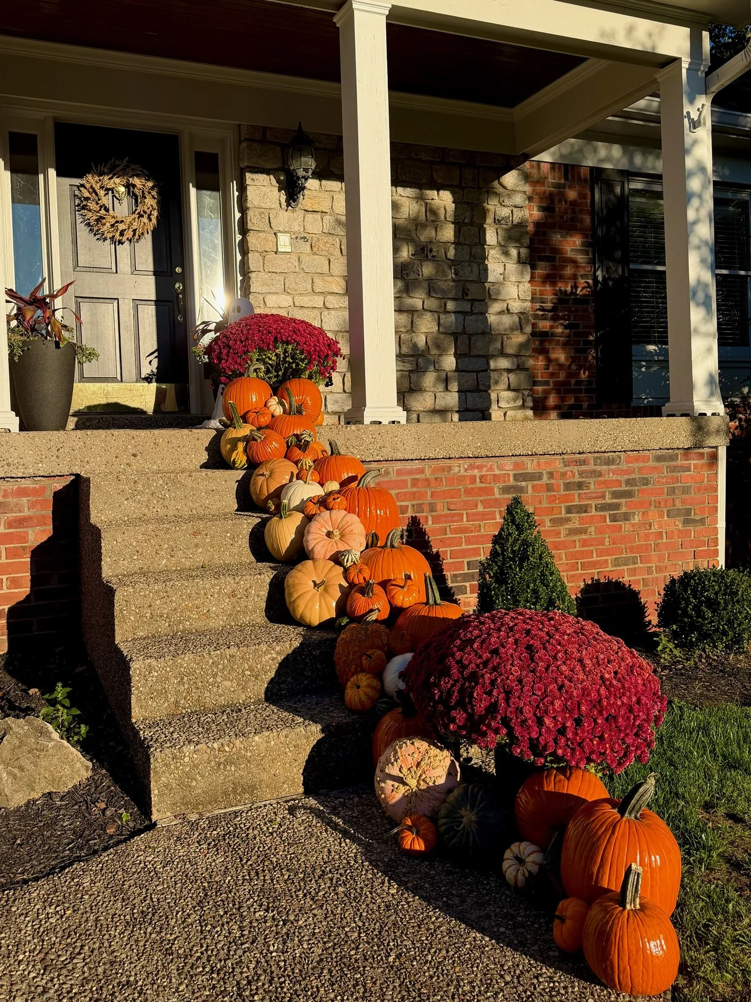 Front porch decorated with pumpkins, colorful mums, and autumn-themed plants on the steps leading to the house entrance.