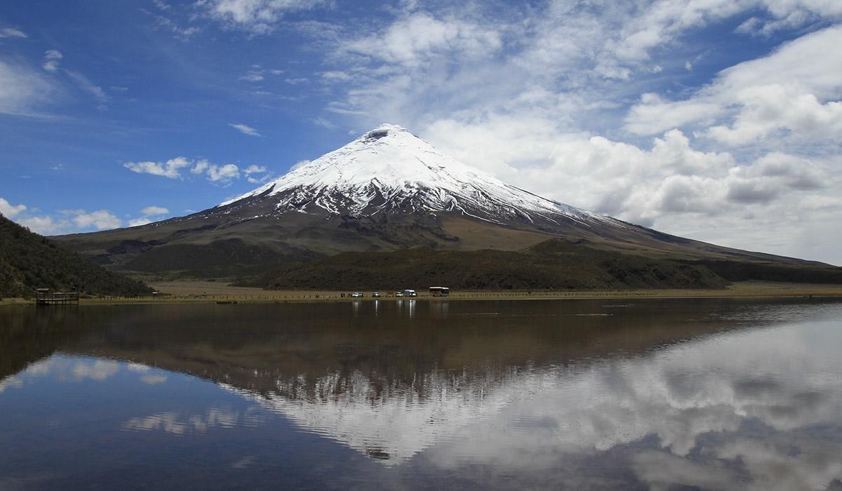 Snow-capped mountain reflected in a lake under a partly cloudy sky.