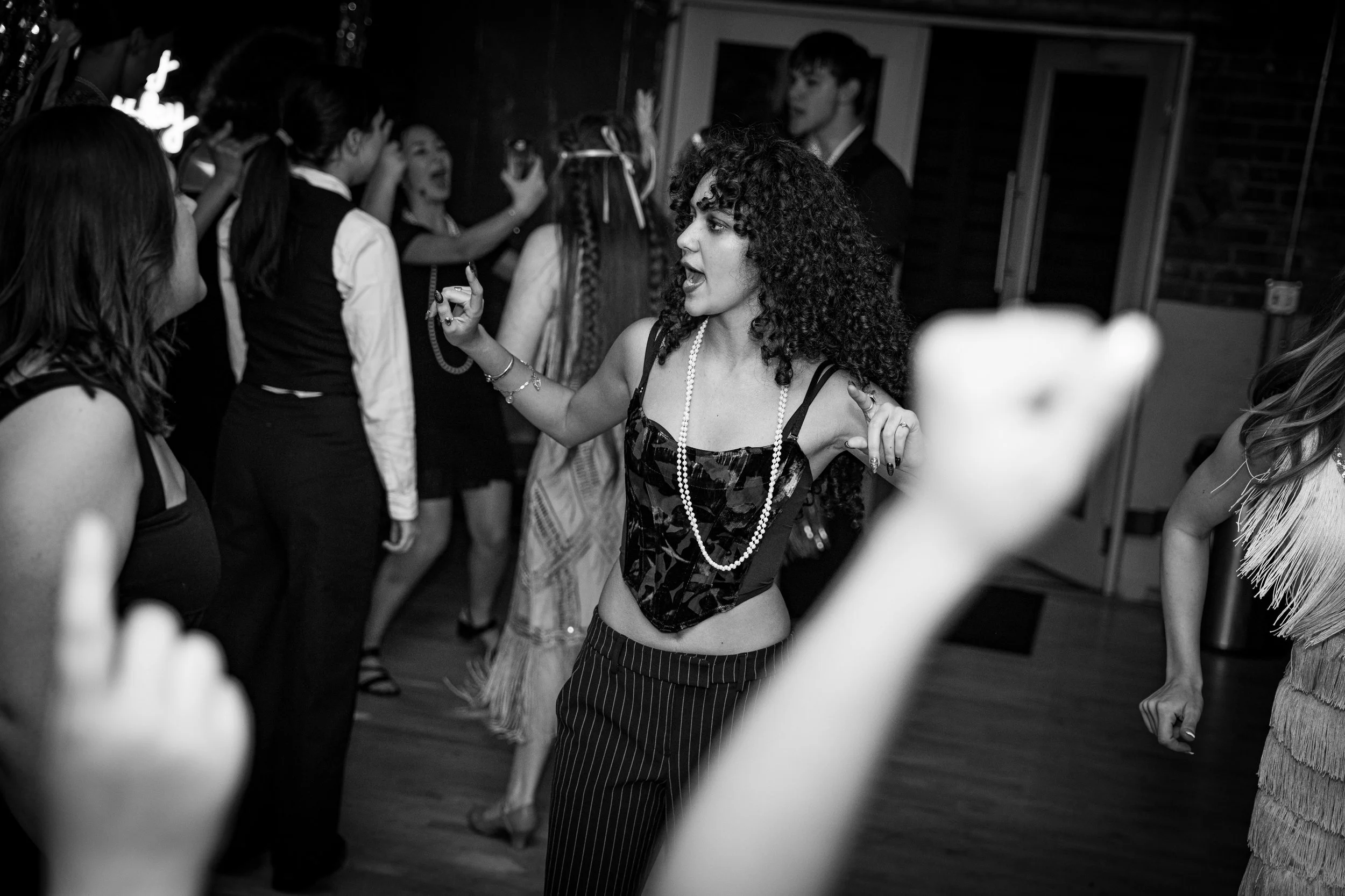 A woman with curly hair dancing and singing at a party, surrounded by other people dancing and celebrating.