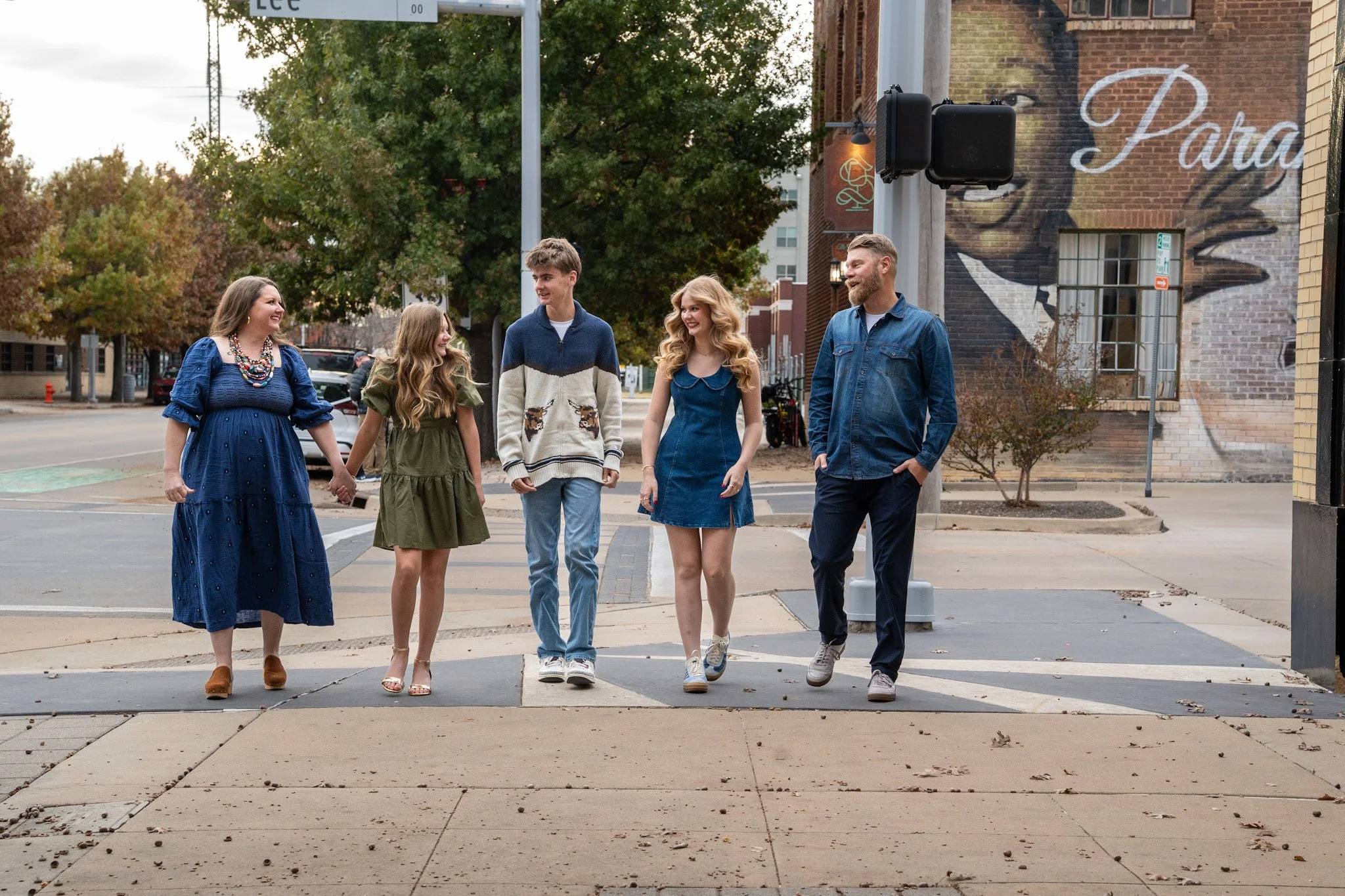 Candid photo of a family walking side by side across a downtown Oklahoma City crosswalk, sharing conversation and natural interaction.