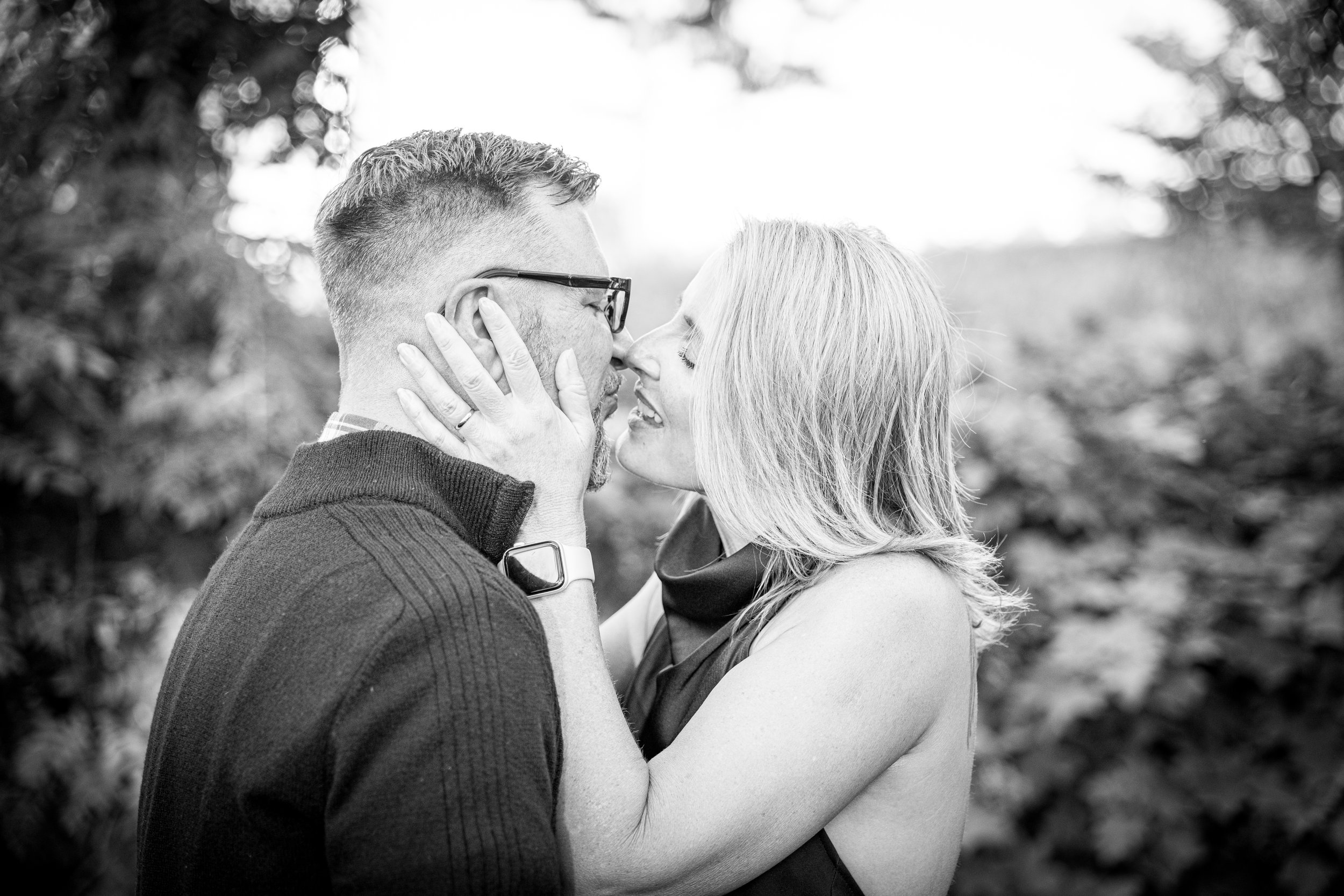 A black and white photo of a couple about to kiss outdoors, with the woman holding the man's face gently.