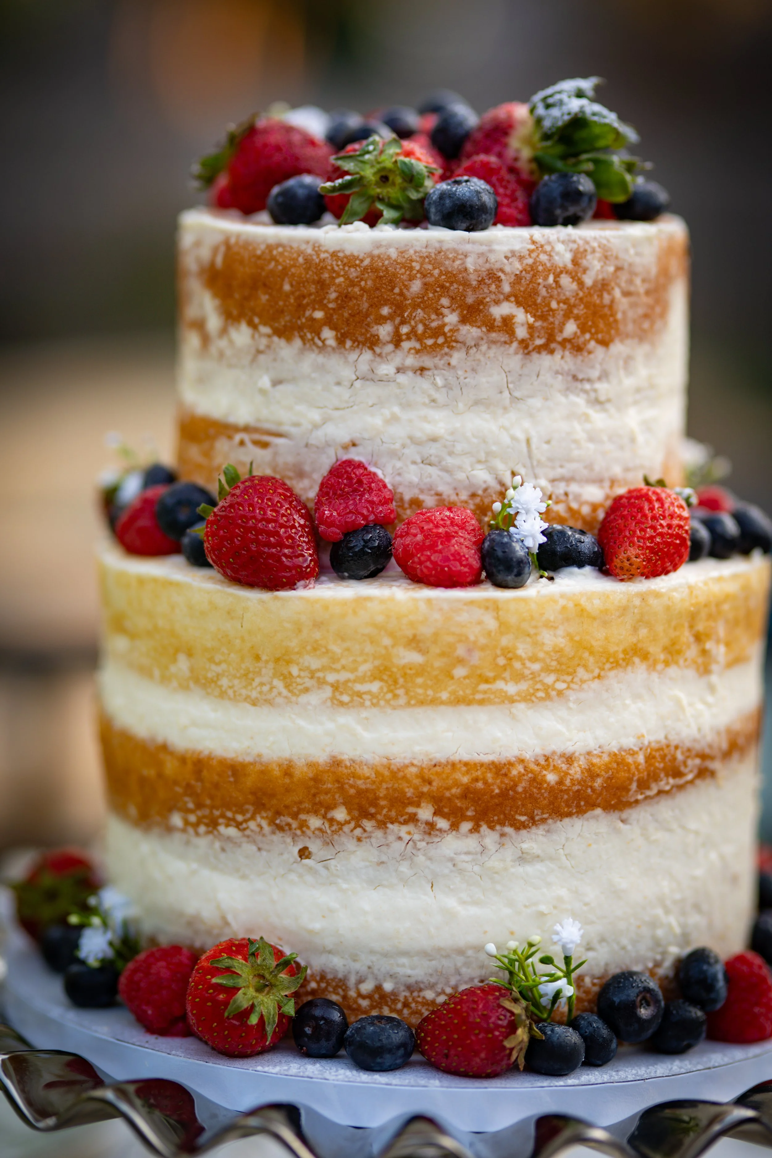 A three-tiered naked cake decorated with fresh strawberries, blueberries, raspberries, and small white flowers.