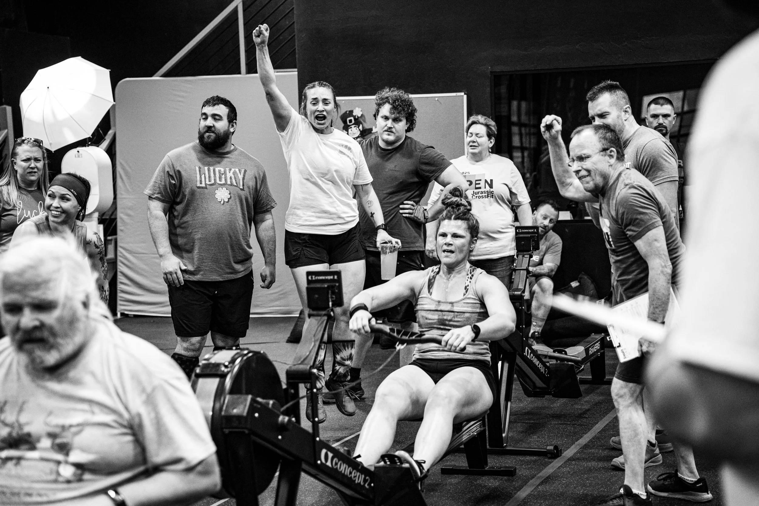 A woman participating in a CrossFit competition using a rowing machine, surrounded by spectators and fellow competitors in a gym.