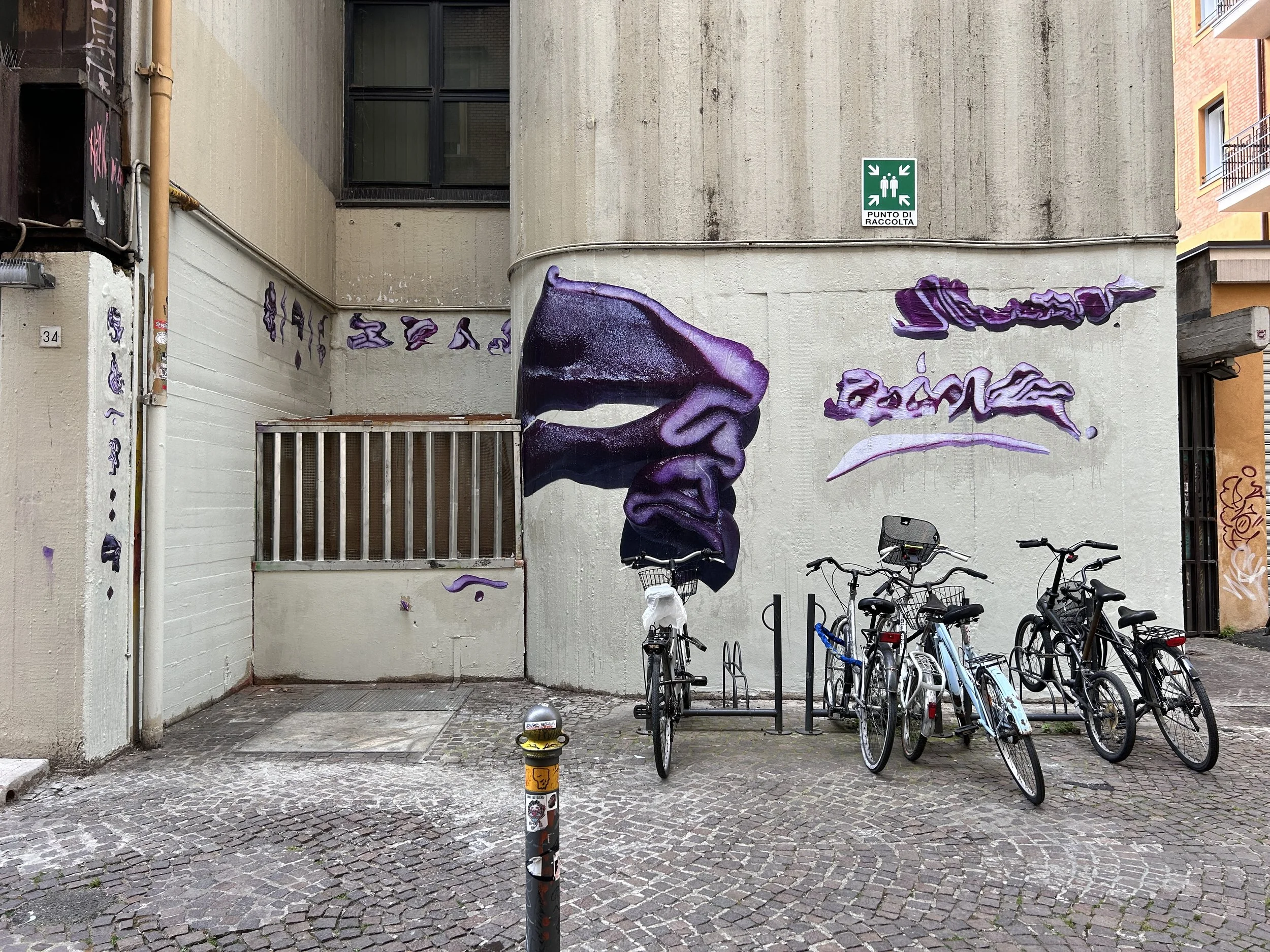 Murale di un gelato di colore viola sulla parete di un edificio, con biciclette parcheggiate davanti e un cartello di sicurezza sulla parete.