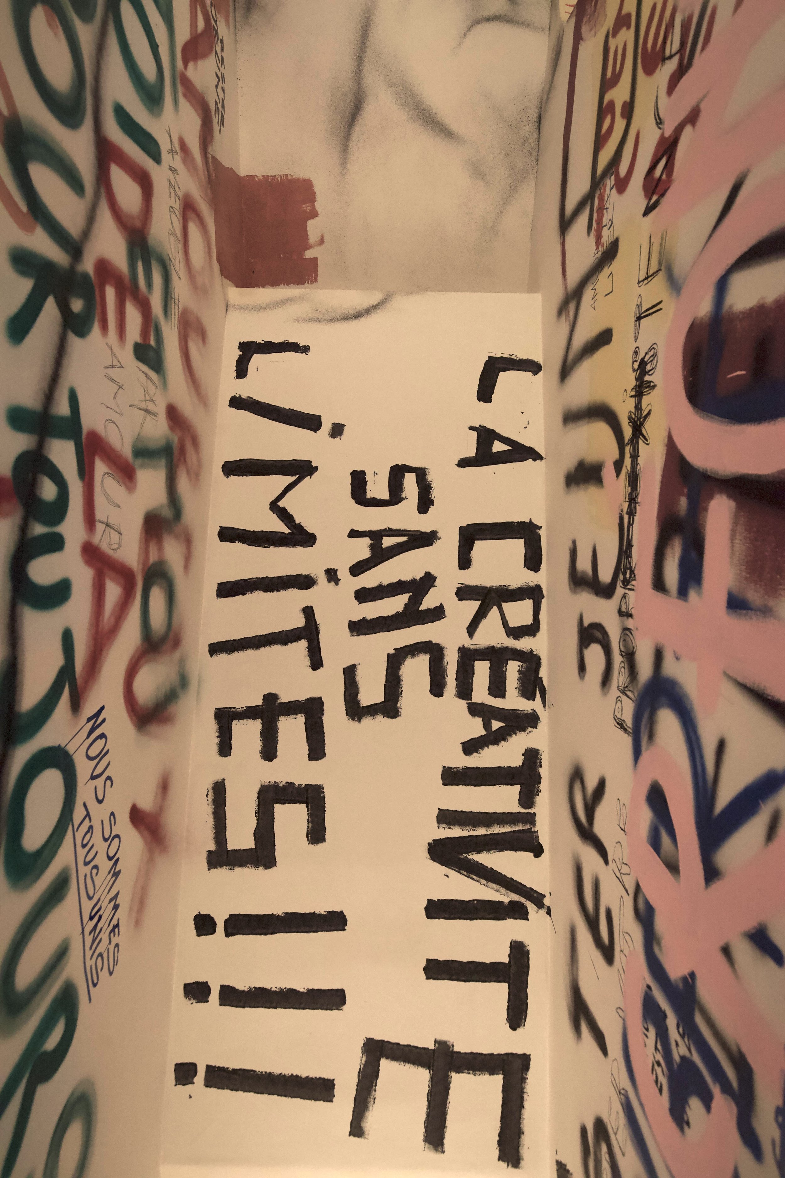 Prospettiva di un cartellone con scritte colorate e in stampatello, con un messaggio scritto a mano, con un muro al centro e decorazioni intorno.