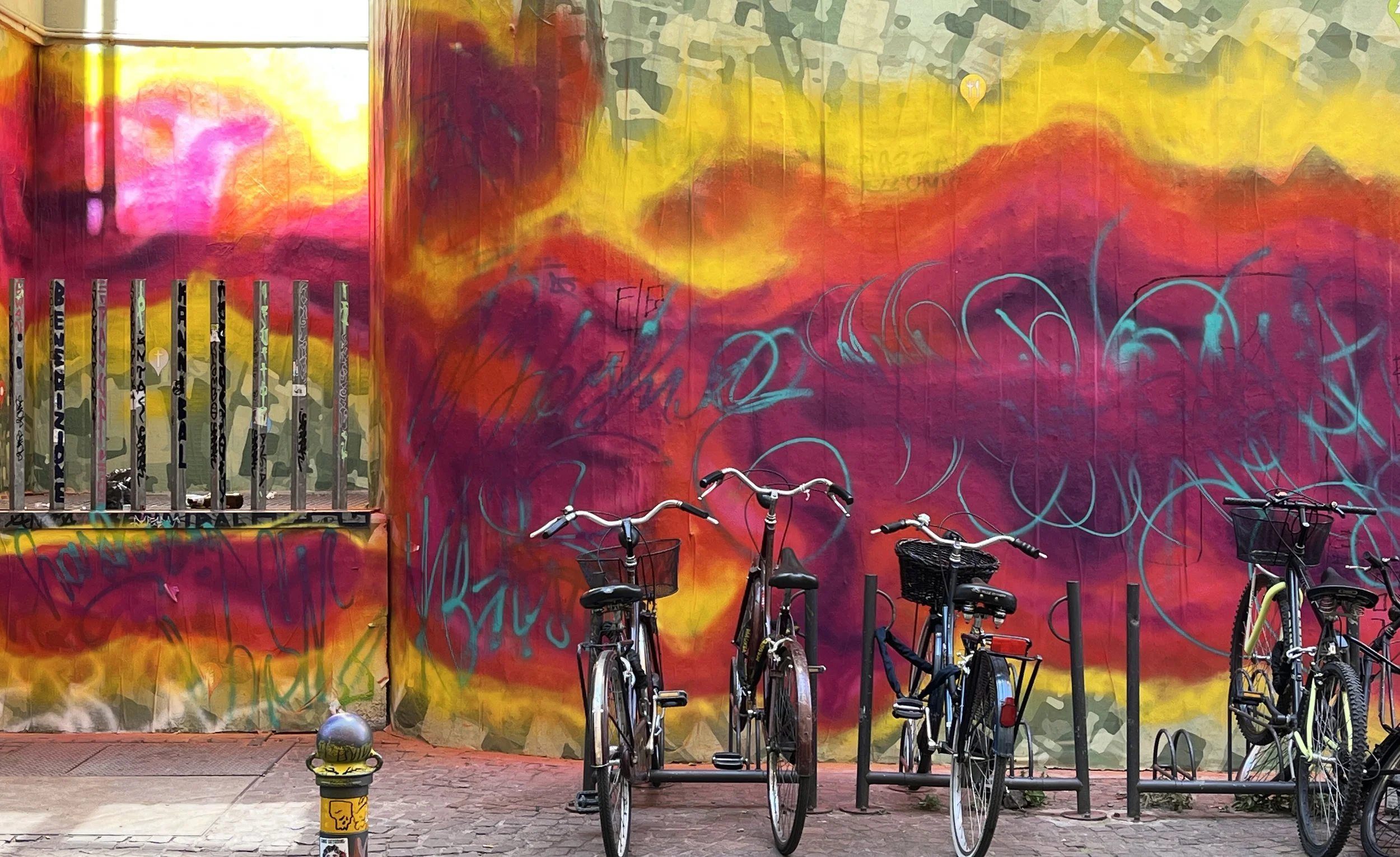Biciclette parcheggiate di fronte a un muro colorato con graffiti e opere d'arte.