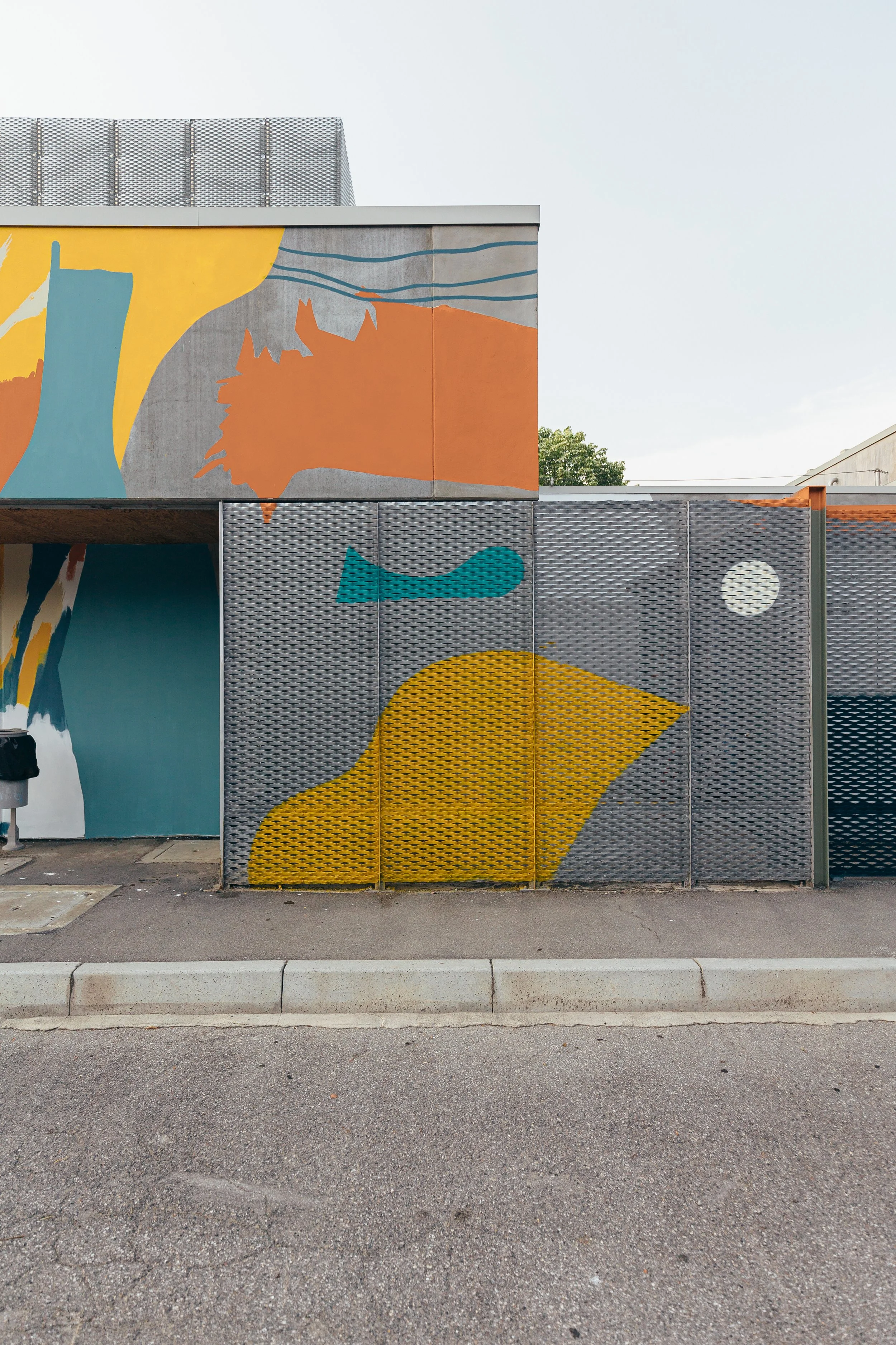 Muro decorato con graffiti colorati e disegni stilizzati di animali e forme astratte, con un pavimento asfalto in primo piano.