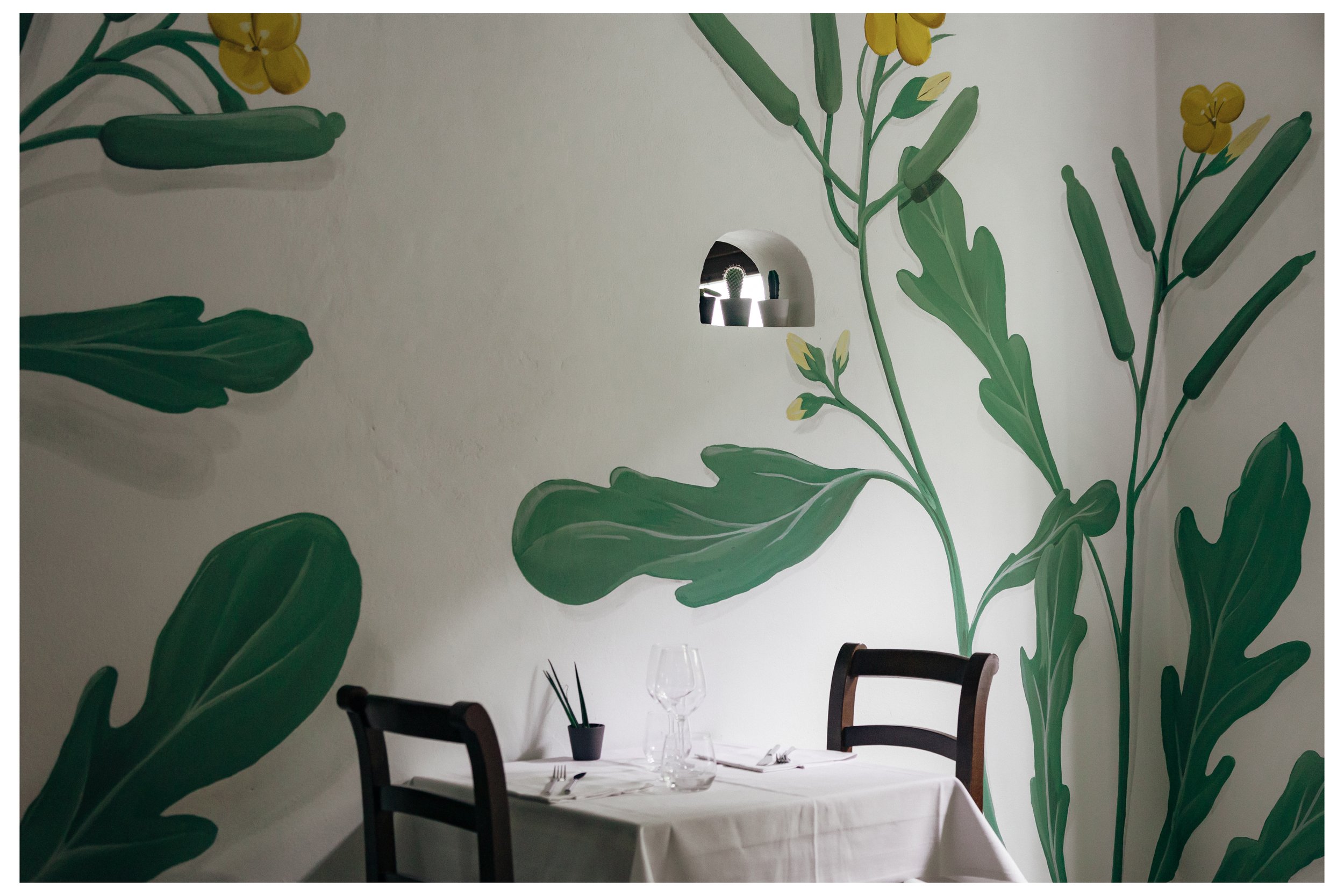 Interno di una sala da pranzo con pareti decorate con grandi disegni di foglie verdi e fiori gialli.