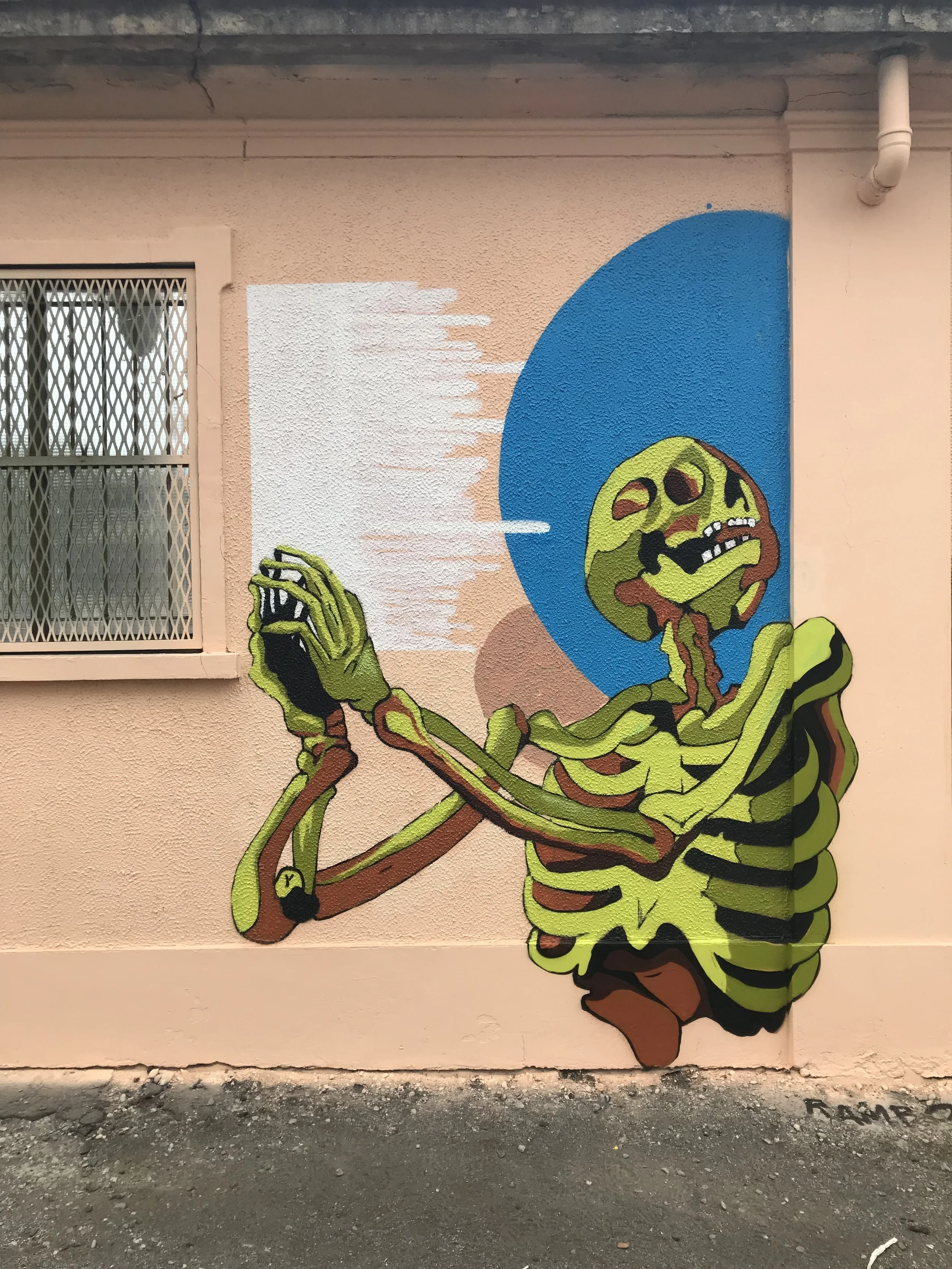 Murale di un robot verde che si gratta la testa, su sfondo multicolore con large cerchio blu.