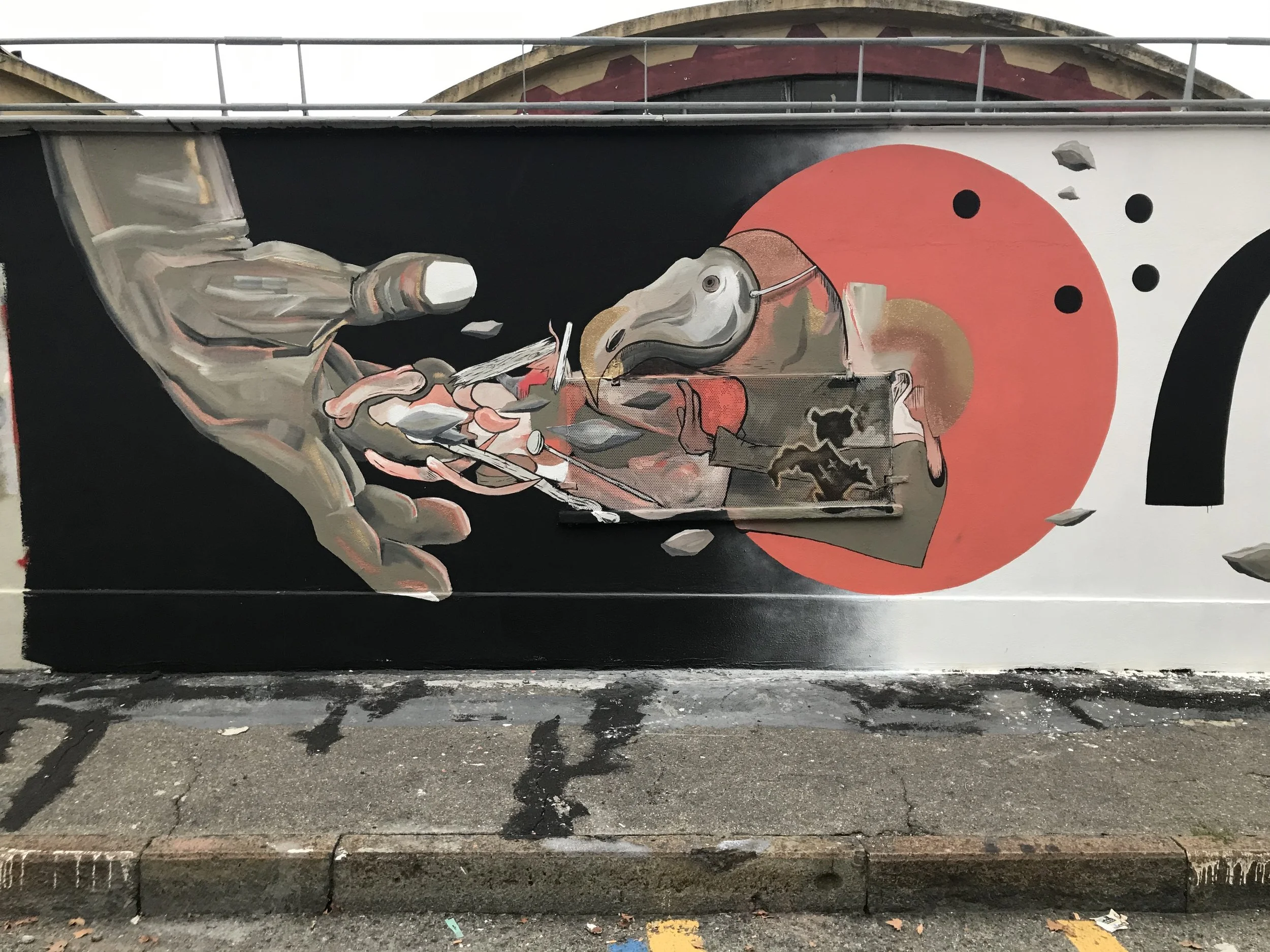 Murale artistica con elementi astratti e geometrici, colori come nero, bianco, rosso, ocra, e sfumature di grigio e beige.