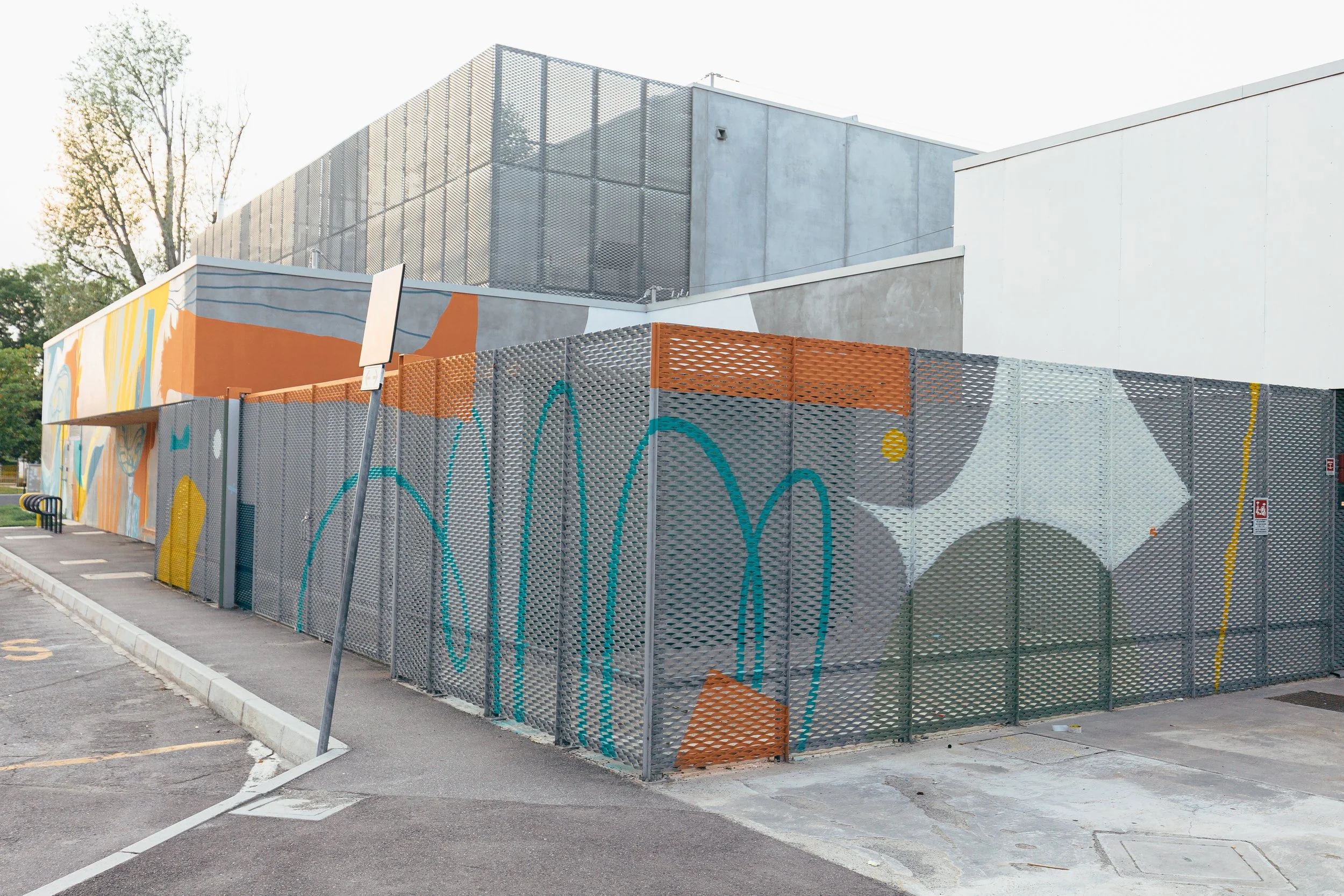 Murale colorata e recinzione metallica che circonda un edificio moderno con pareti di cemento e dettagli in metallo.