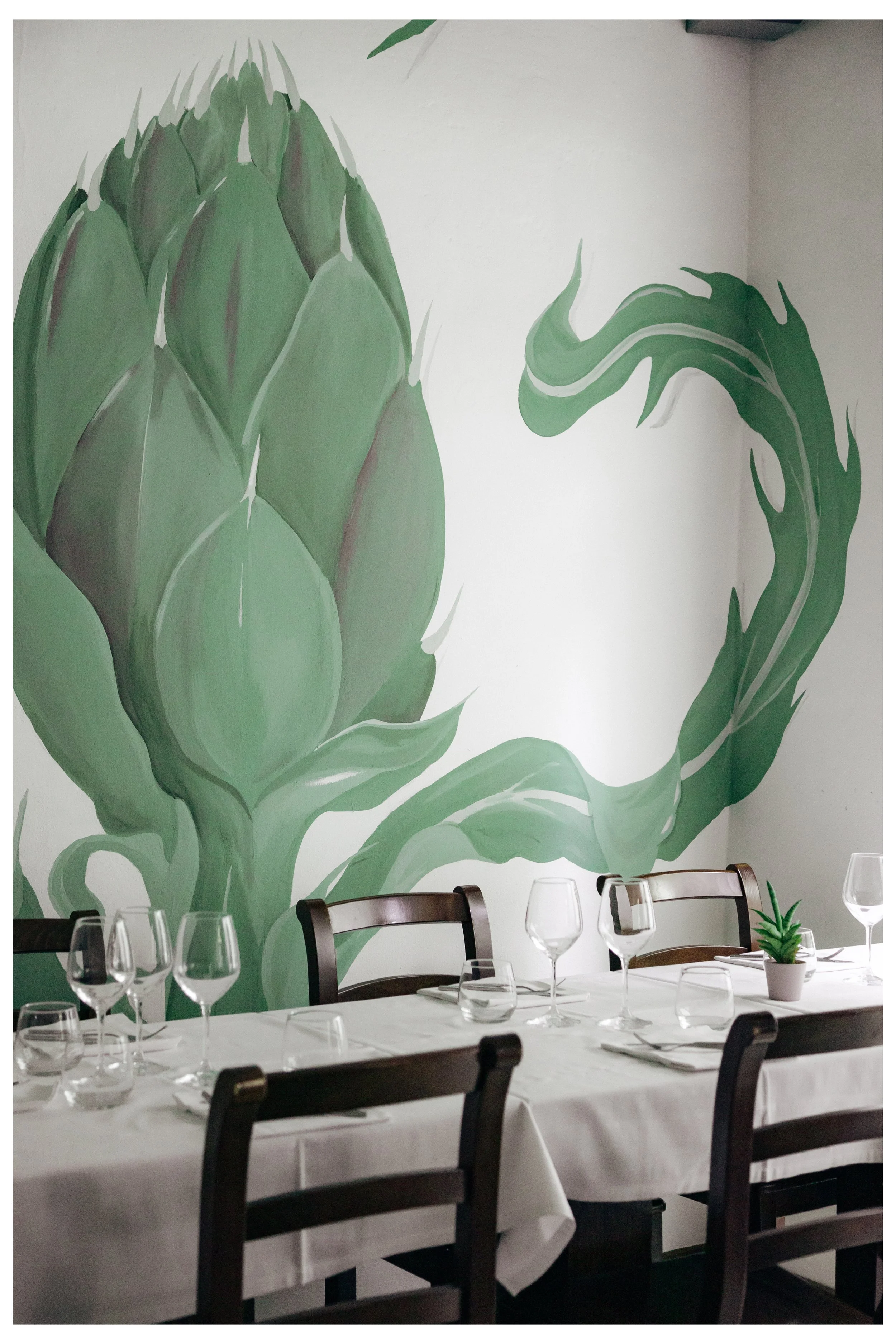 Dipinto murale raffigurante un grande cespuglio di piante di asparagi, decorativo interno di ristorante con tavolo apparecchiato con bicchieri e pianta in vaso.