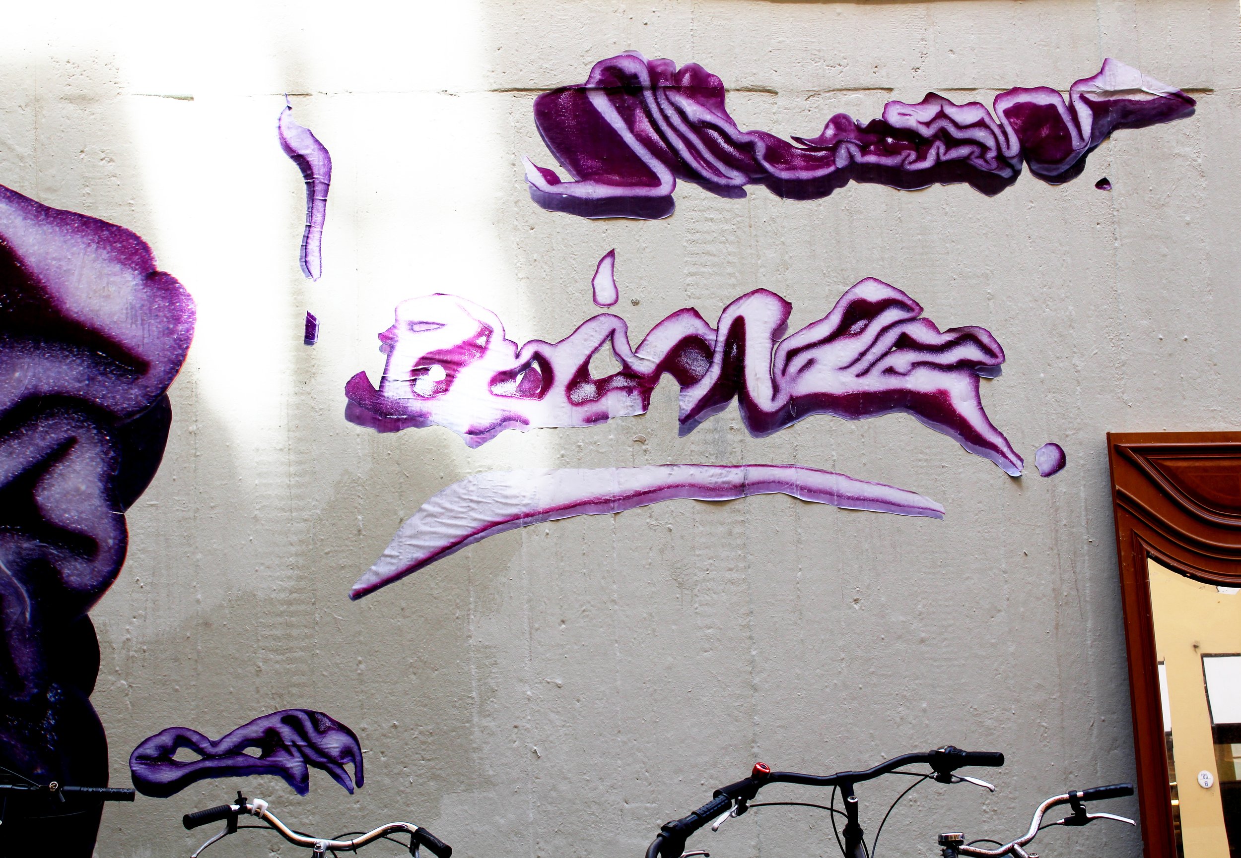 Strisce di plastica o tessuto viola appese su un muro beige, alcune con disegni reticolari, altre lisce.