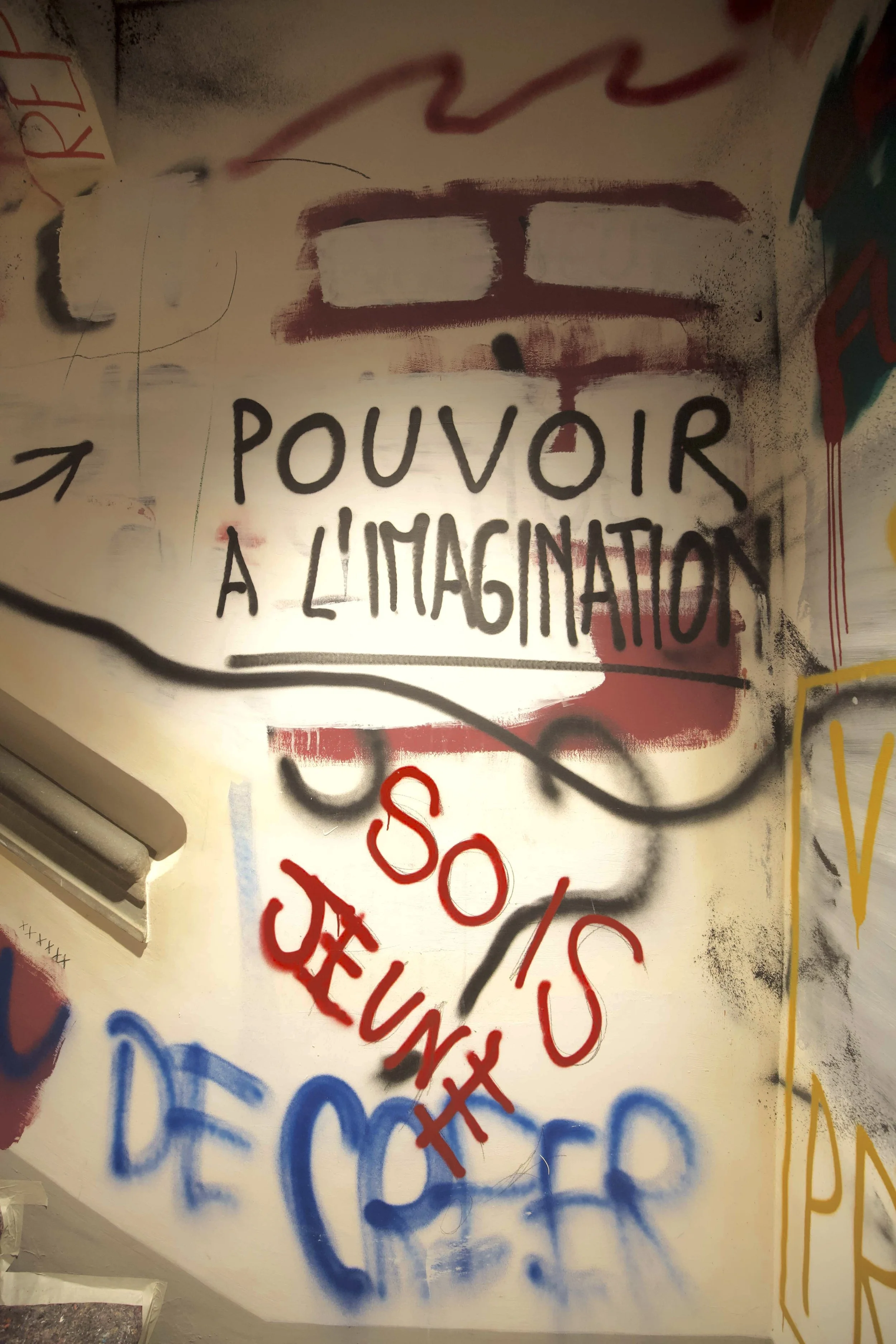 Murale con scritte spray con frase in francese, come 'POUVOIR A L'IMAGINATION', e disegni astratti e graffi colorati.