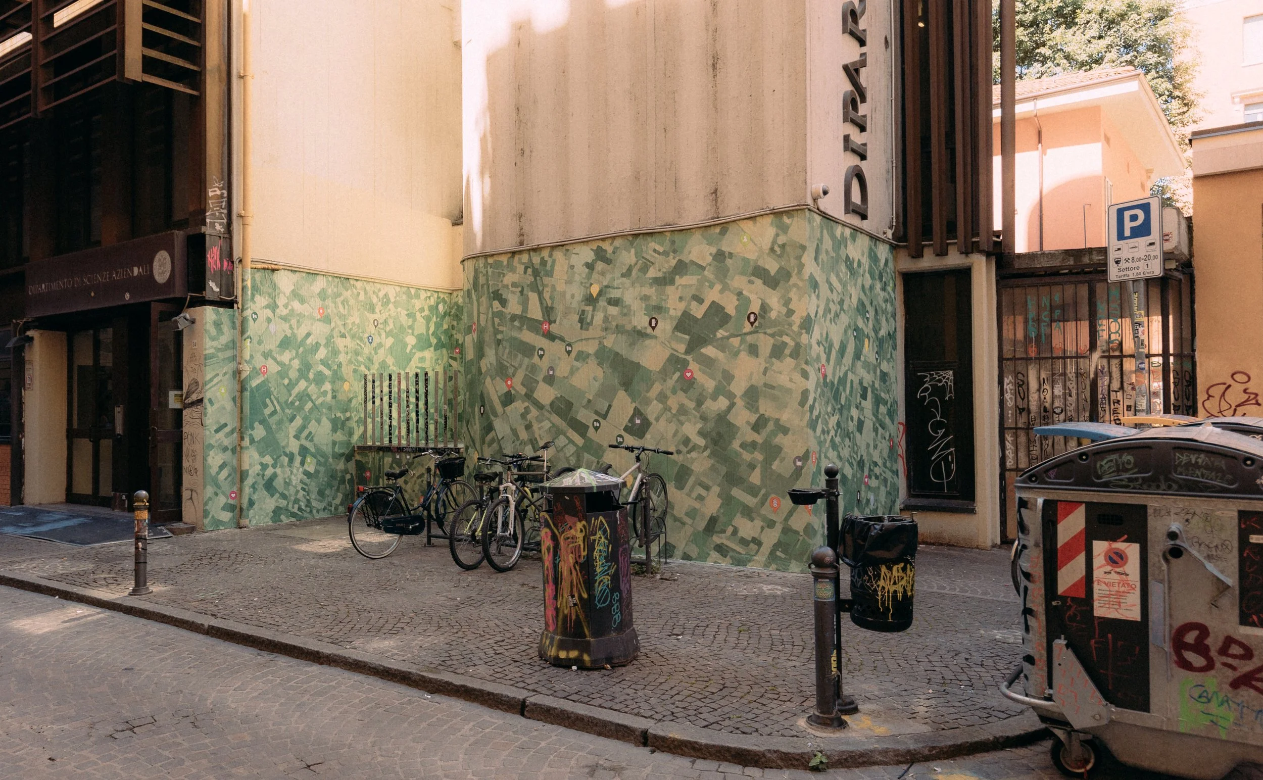 Muro decorato con mappa della città, biciclette parcheggiate, bidoni della spazzatura e mobili urbani in centro città.