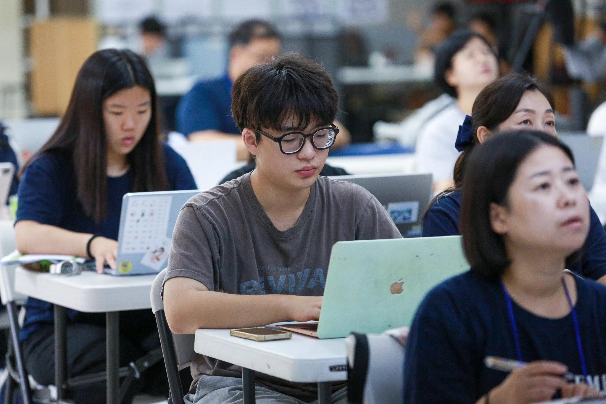 Young people sitting at desks in a classroom, working on laptops.