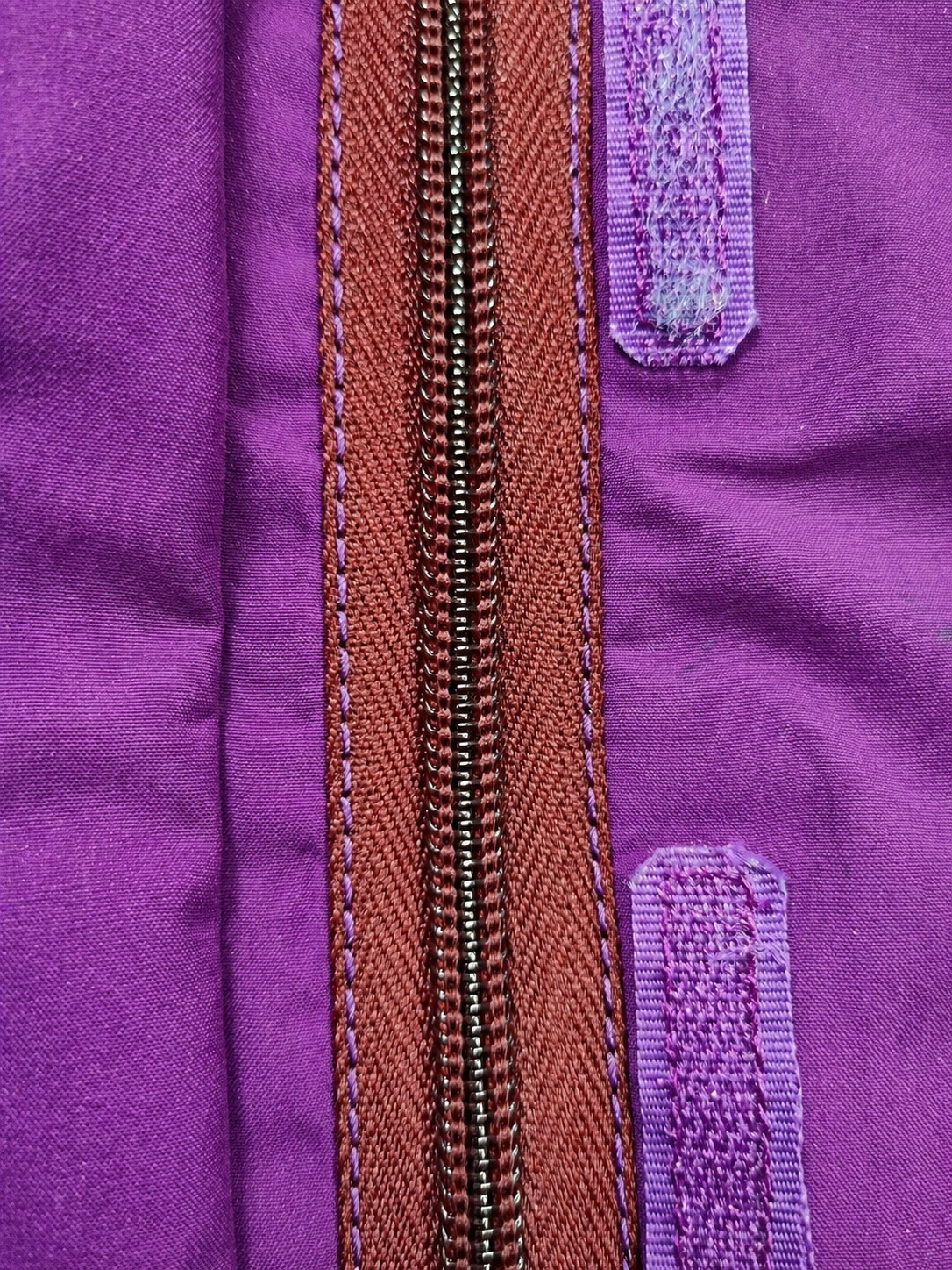 Close-up of a purple jacket with a brown zipper and purple Velcro strips on each side of the zipper.