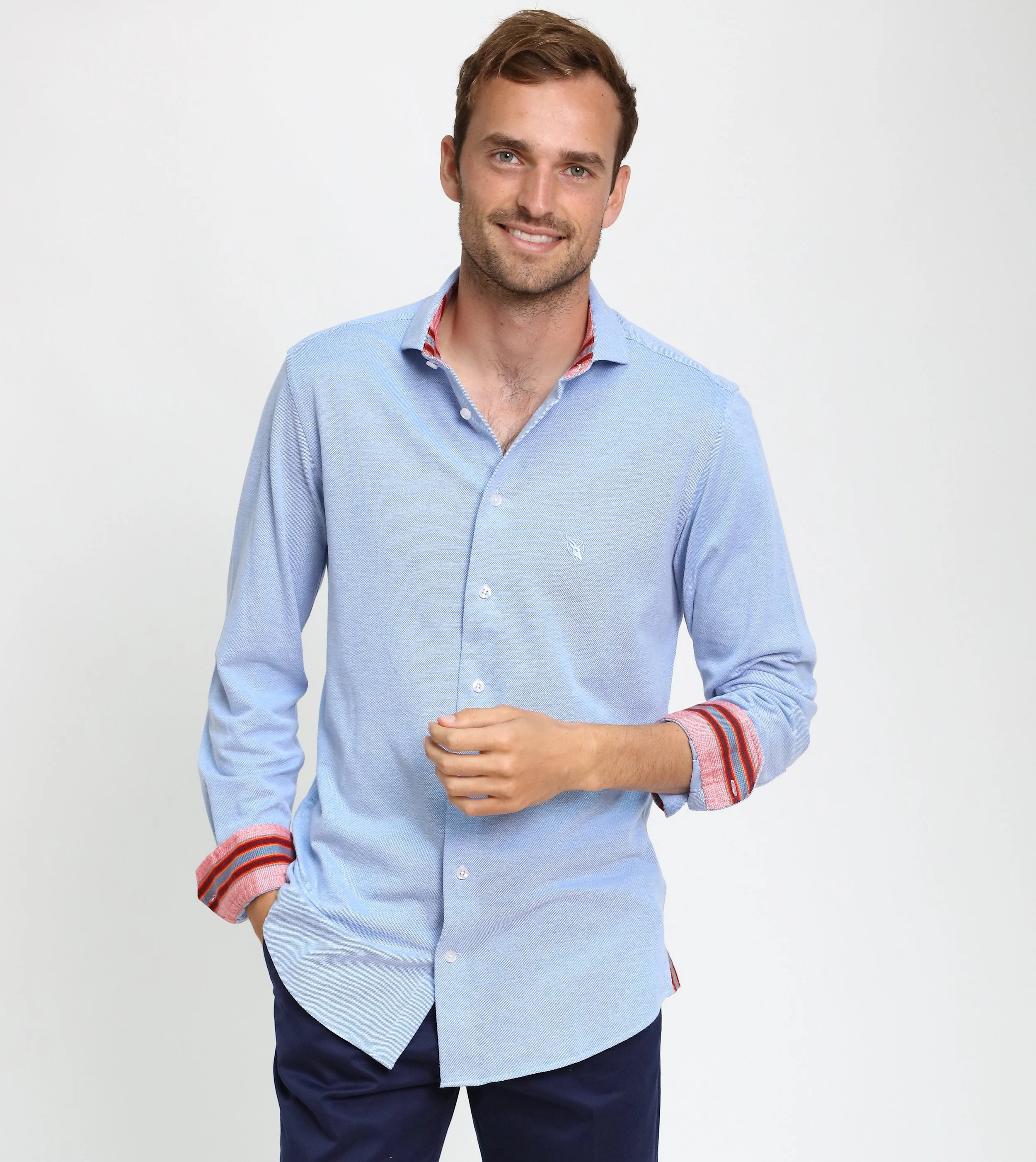 Smiling young man in a light blue button-up shirt with red and orange accents on the collar and cuffs, standing against a plain white background.