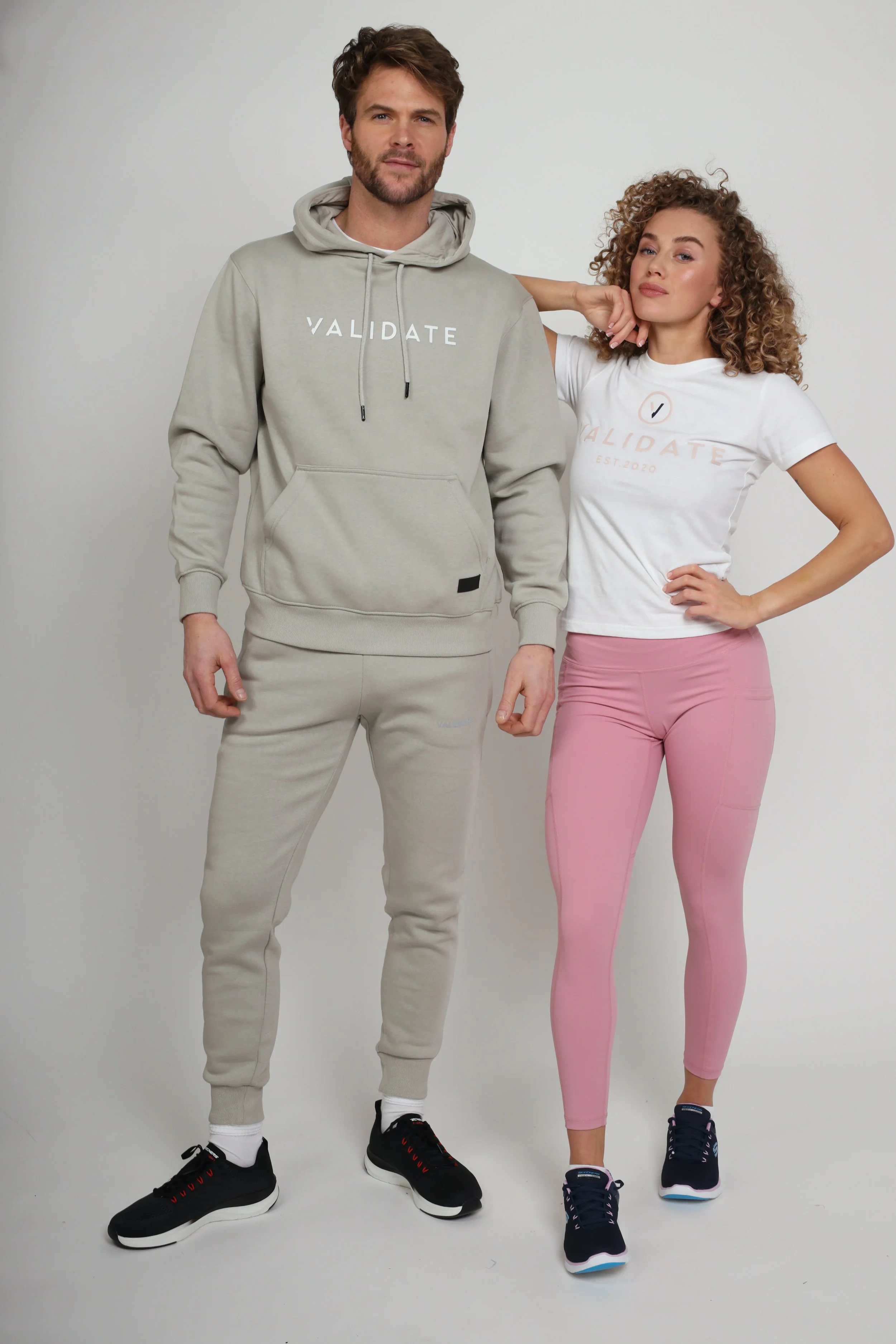 A man and woman standing side by side against a plain background, wearing casual athletic clothing with the word "VALIDATE" on their shirts.