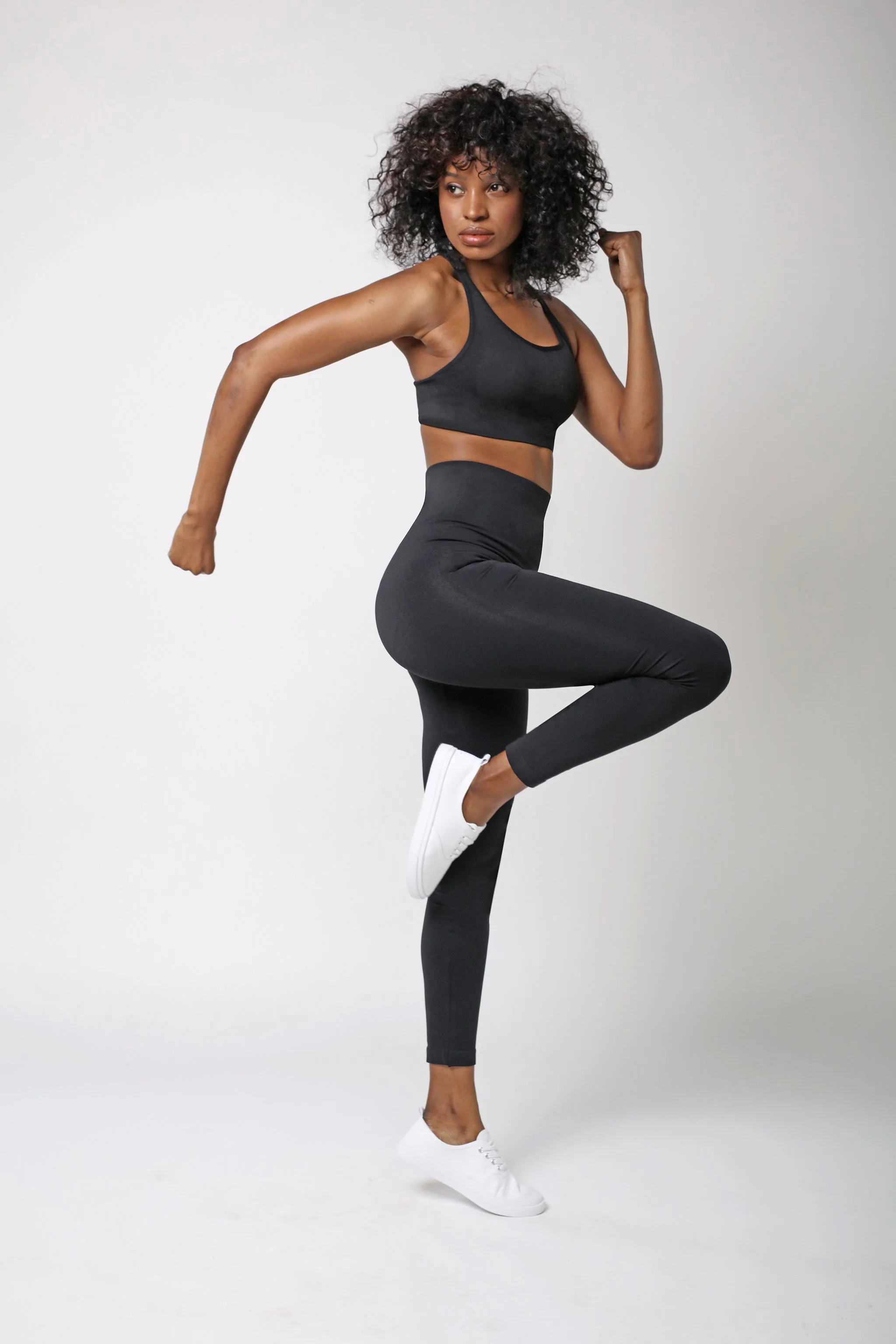 A woman in black workout attire performing a side balance pose, with one arm flexed and one leg raised, against a plain white background.