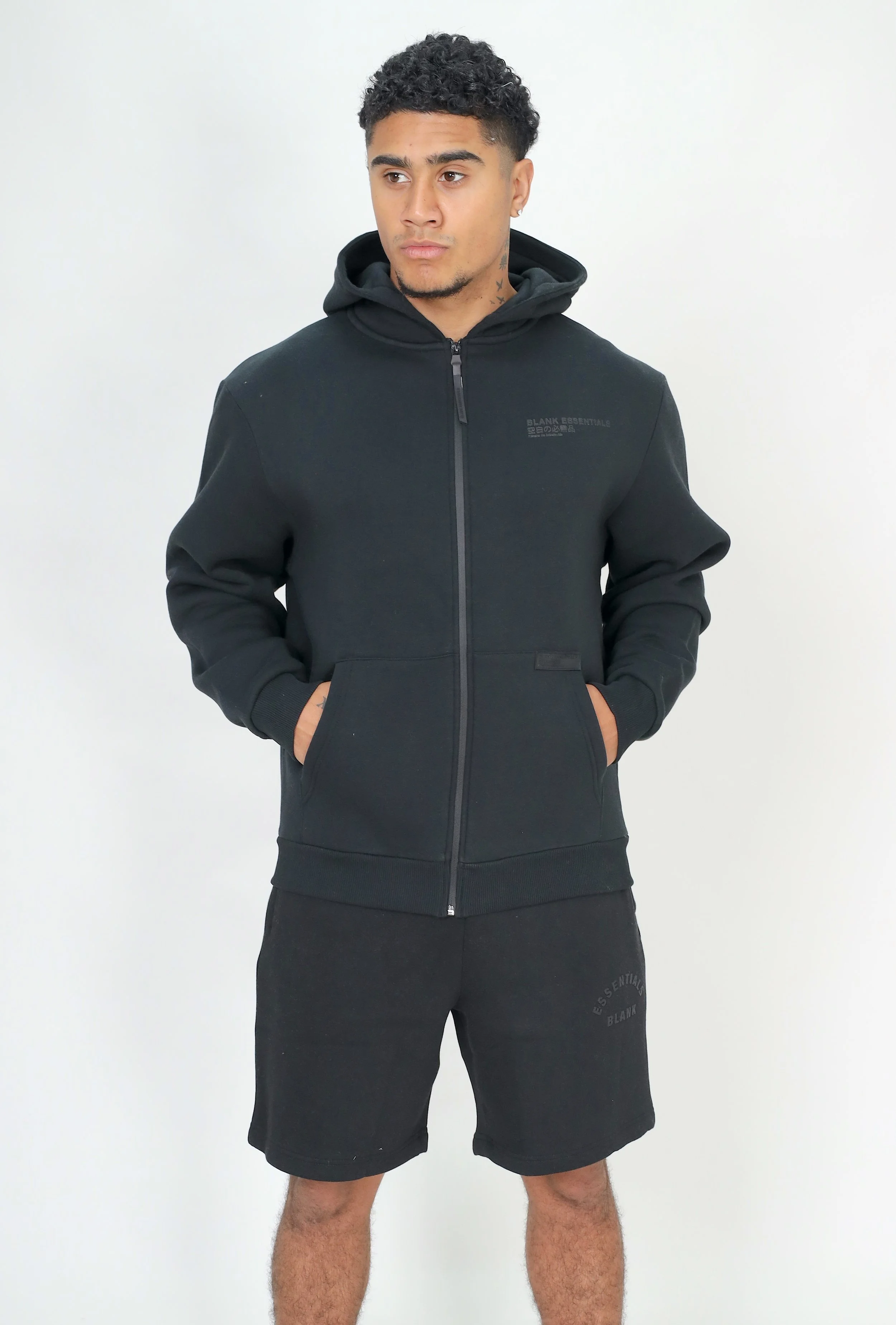 Young man in black hoodie and shorts standing against a plain white background.