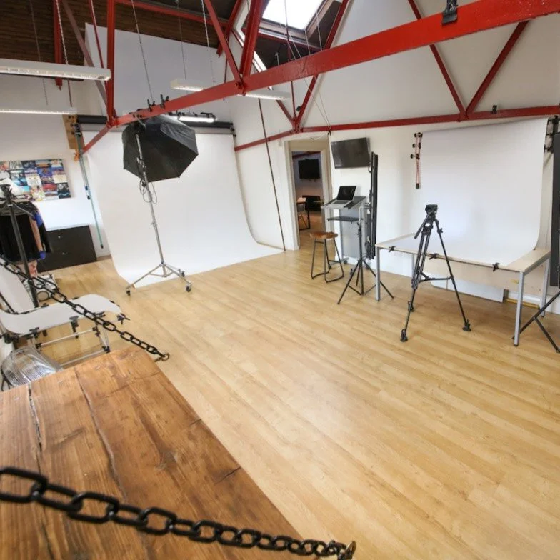 Lighting and filming equipment in a photography studio with a wooden floor and white walls.