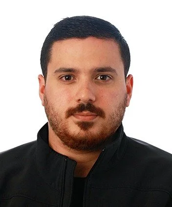 Headshot of a young man with dark hair and beard wearing a black jacket against a plain white background.