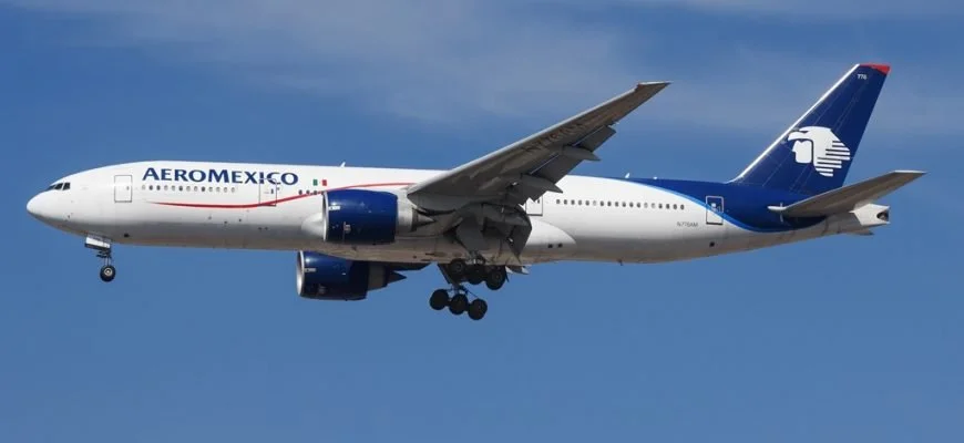 A commercial airplane in flight with AeroMexico branding on the fuselage and a blue tail fin with a white eagle logo, flying in a clear blue sky.