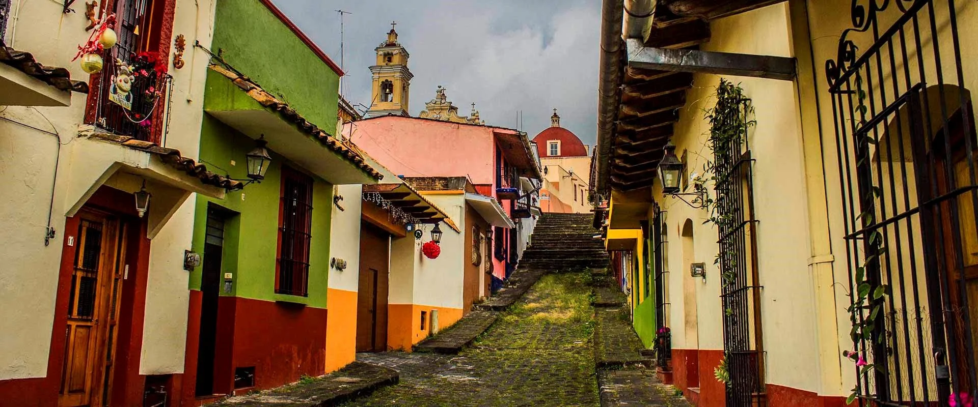 Colorful houses on a cobblestone street with hill steps, with church towers in the background.