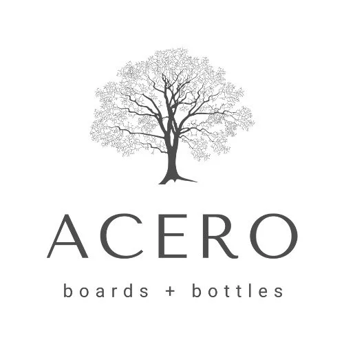 A logo with a black silhouette of a leafless tree and the text "ACERO" below it, followed by "boards + bottles" underneath.
