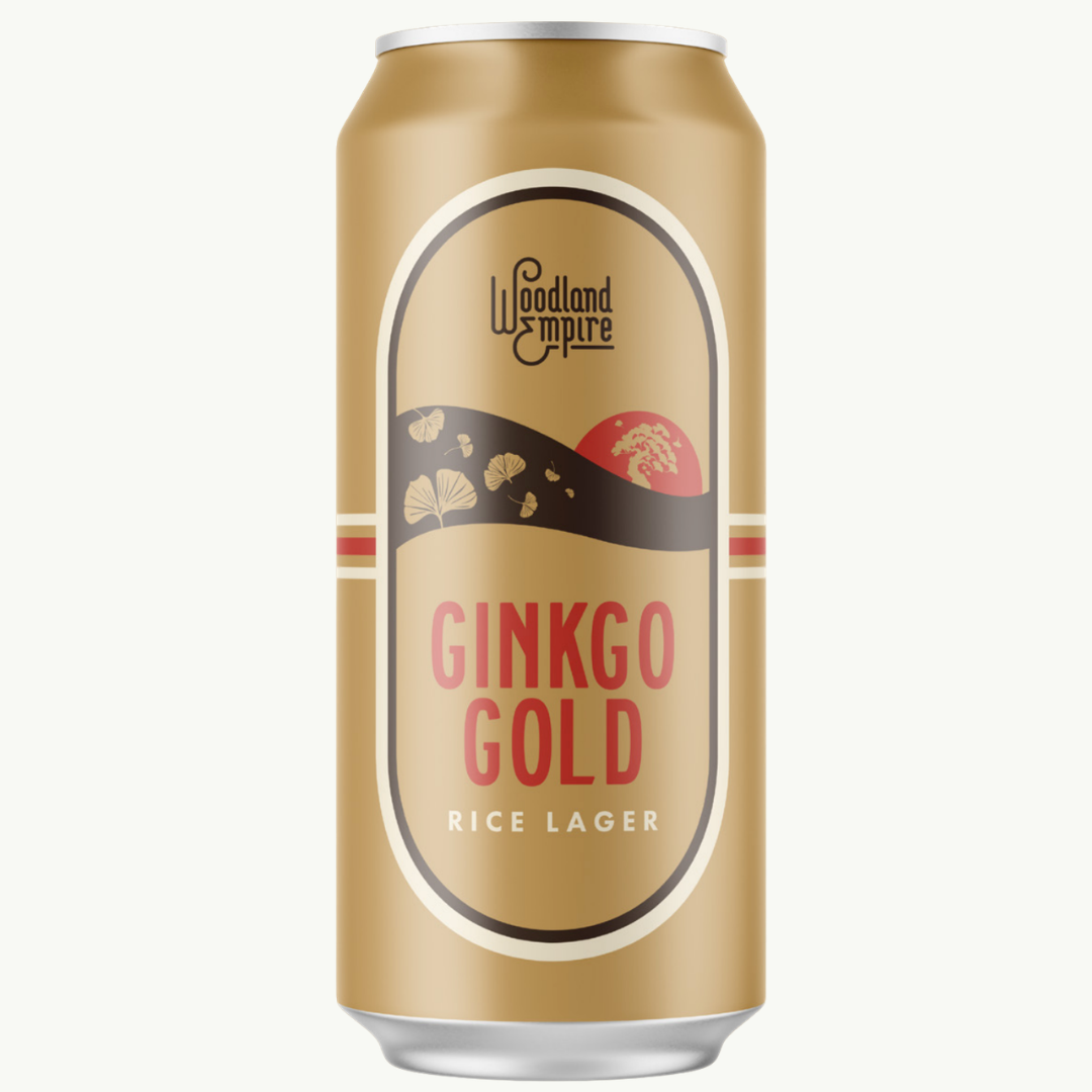 A gold-colored can of Woodland Empire Ginkgo Gold Rice Lager with a label featuring stylized ginkgo leaves, a red sun, and red and white stripes.