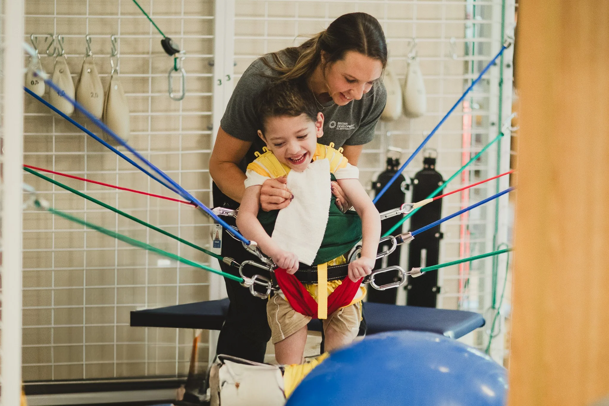 A therapist assists a young child wearing a TheraSuit as part of a pediatric physical therapy session using supportive equipment.