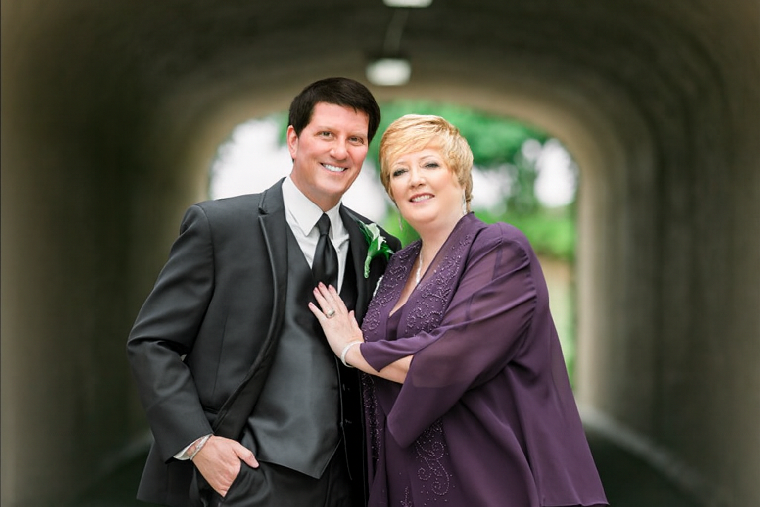 A couple stands together smiling beneath an archway, capturing a moment of partnership, support, and shared commitment.
