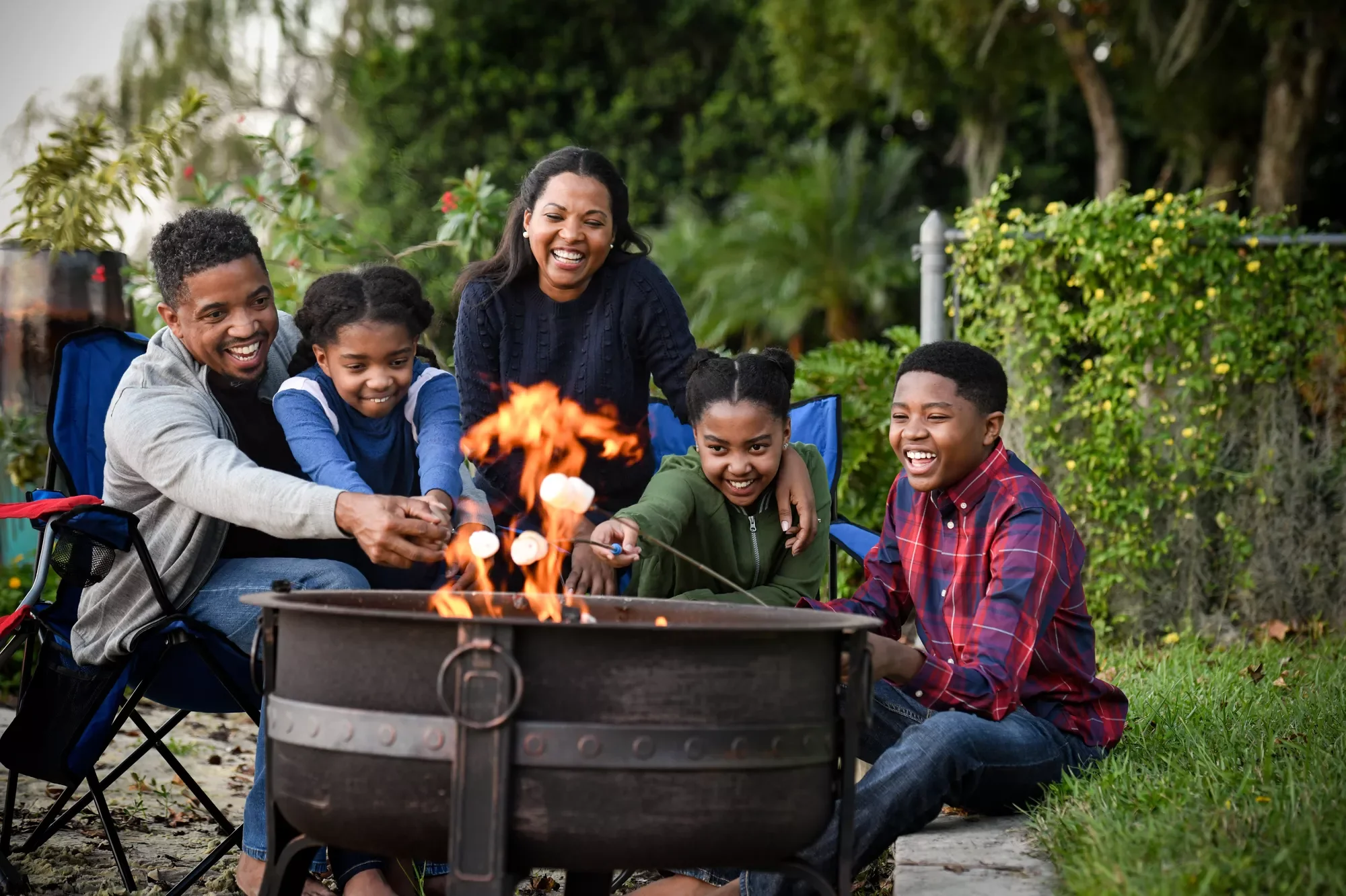 A family gathers outdoors around a fire pit, smiling as they roast marshmallows together.