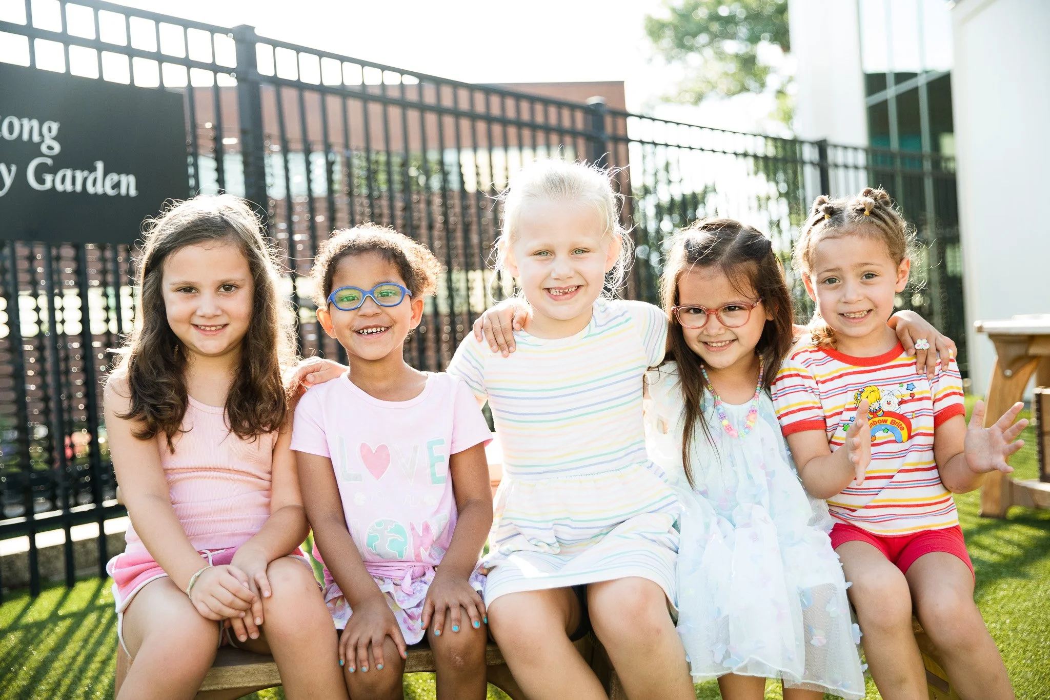 Five young children sit together smiling outdoors, reflecting friendship, inclusion, and joyful connection.