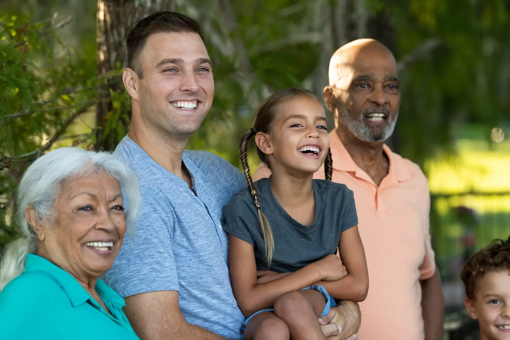A smiling four-generation family stands together in a park, capturing warmth, connection, and shared well-being.