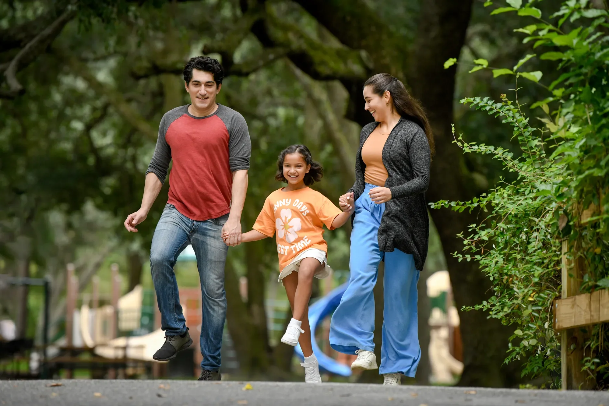 A family of three, consisting of a man, a woman, and a young girl, walking together in a park.