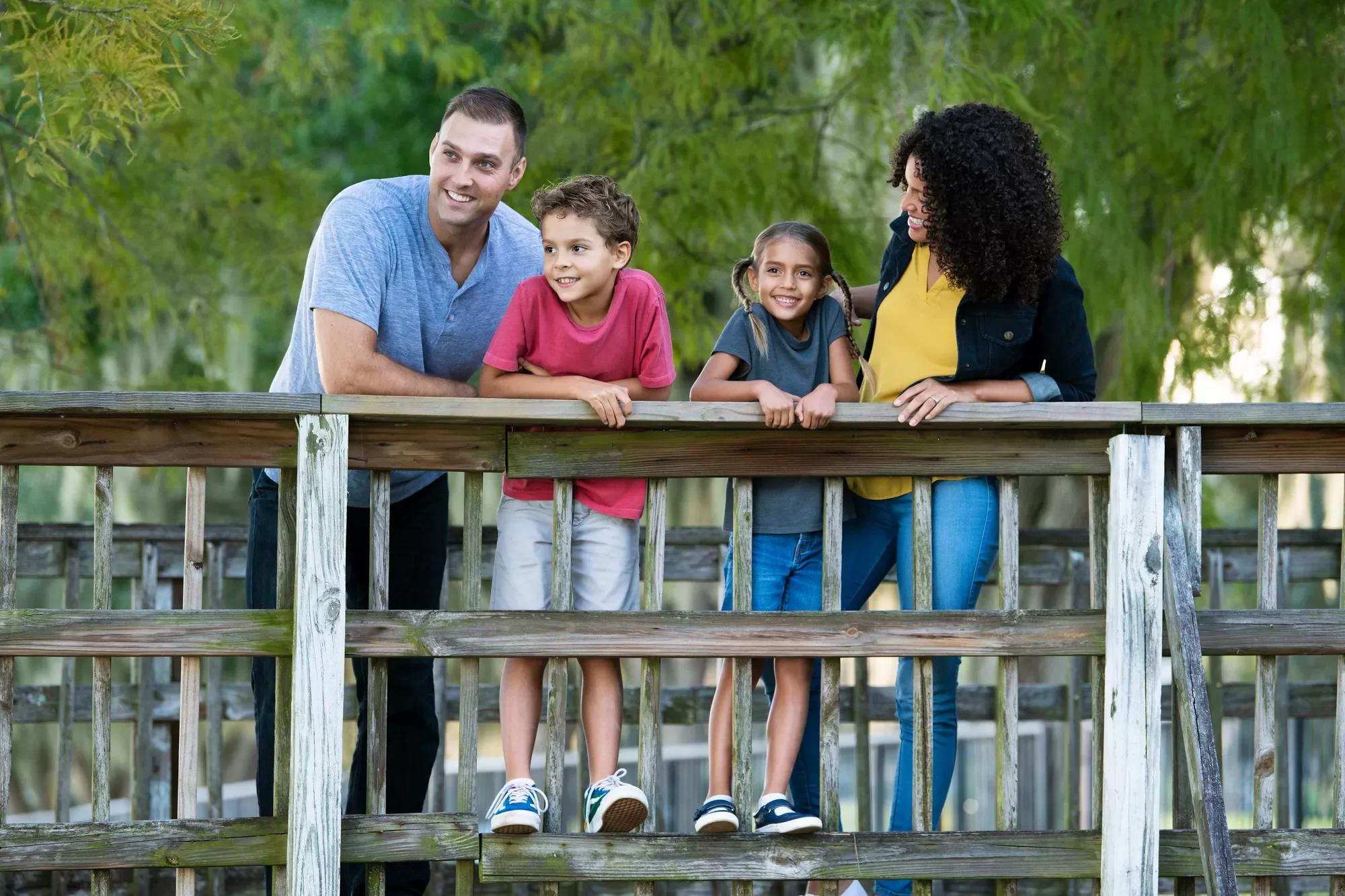 A smiling family of four stands together on a wooden deck, enjoying the outdoors.