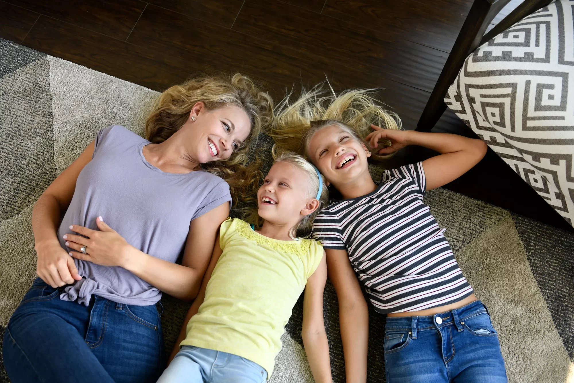 A mother and her two daughters are lying on the floor, smiling and laughing.