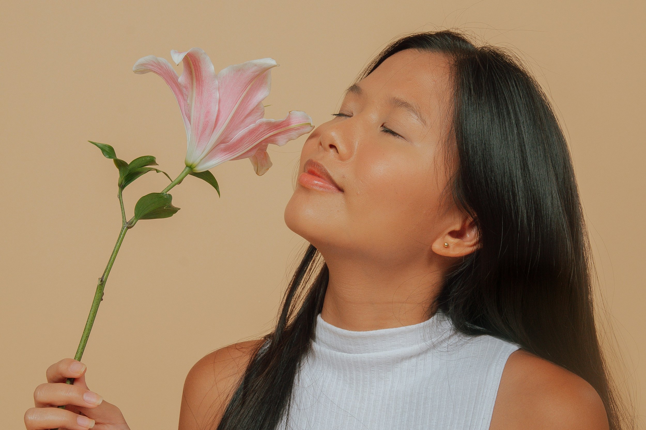 Asian woman with eyes closed holding and smelling single pink flower