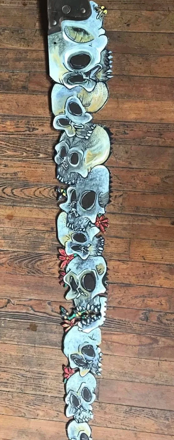A vertical row of painted animal skulls with floral and insect decorations on a wooden floor.