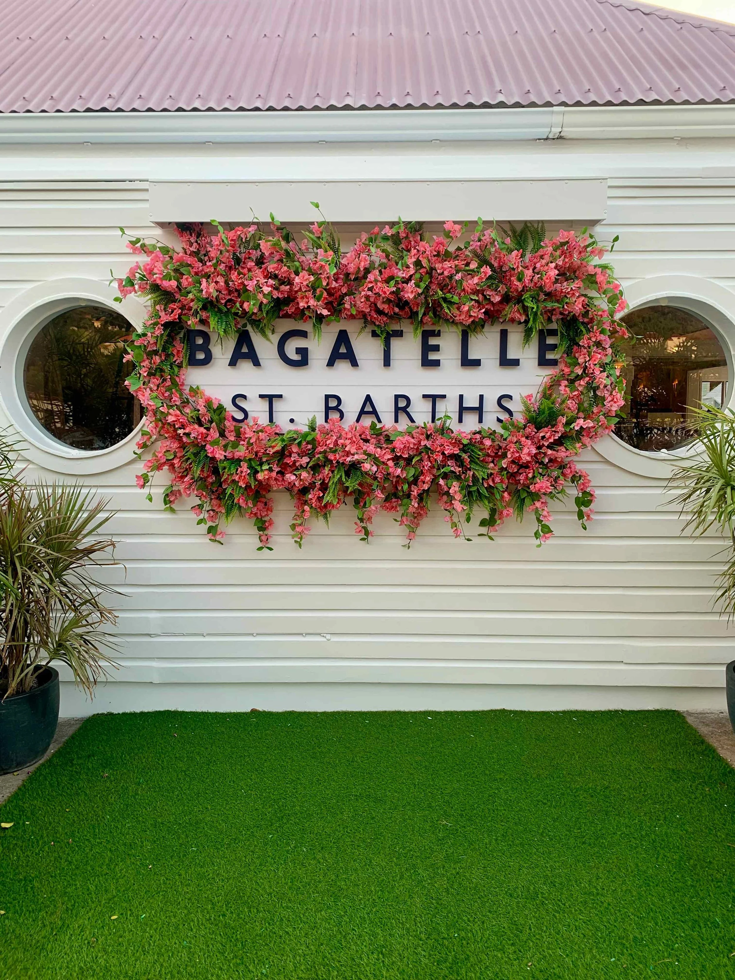 Sign reading ‘Bagatelle St. Barths’ surrounded by pink flowers and greenery, with a house in the background in St Barth.