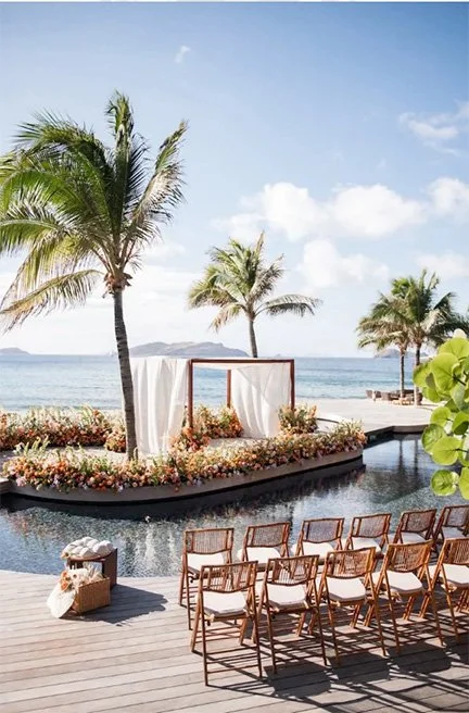 Elegant seaside wedding ceremony with floral arch, tropical palm trees, and ocean backdrop in St Barth.
