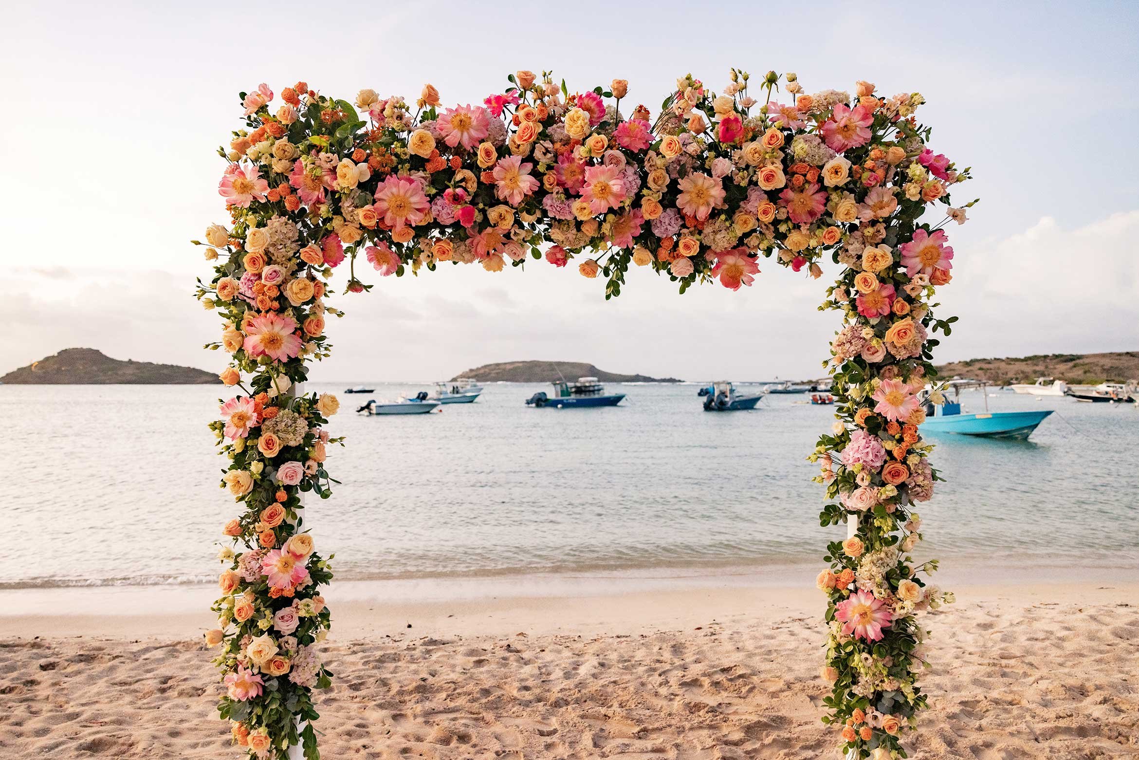 Peach and pink floral wedding arch on the sand with turquoise sea views in St Barth.
