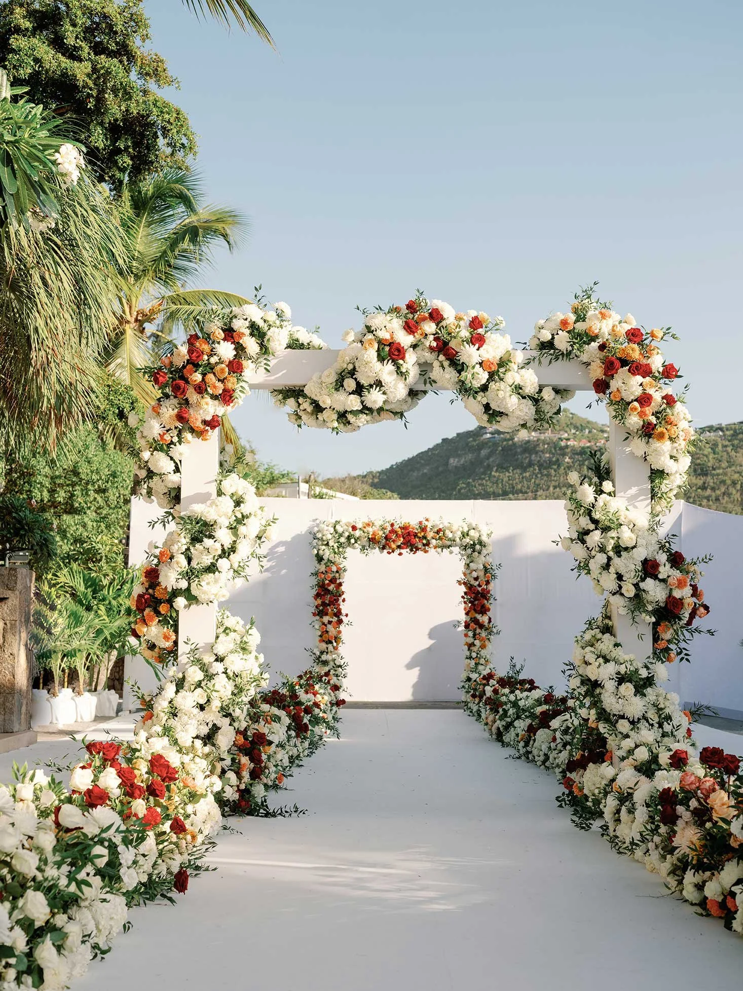 Vibrant tropical wedding arch in red and white, surrounded by lush greenery for an exotic ceremony in St Barth.