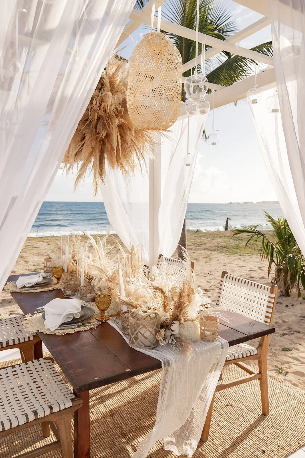 Bohemian outdoor dinner setup by the sea with white linens, candles, and green plants, creating an elegant and relaxed wedding atmosphere in St Barth.