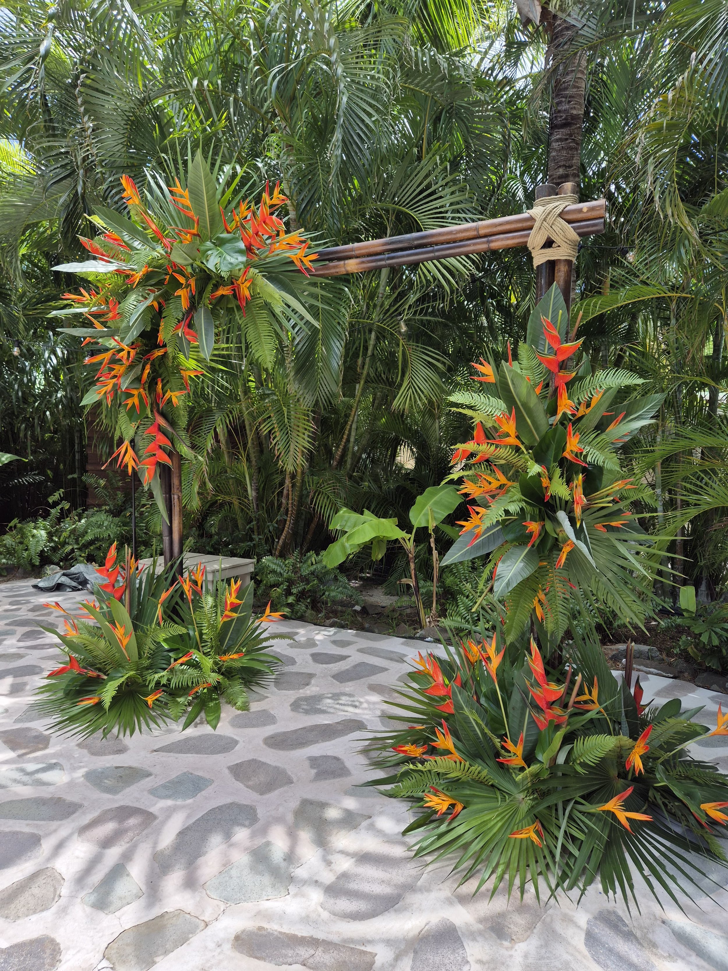 Vibrant tropical wedding arch with orange and green flowers surrounded by lush greenery in St Barth.