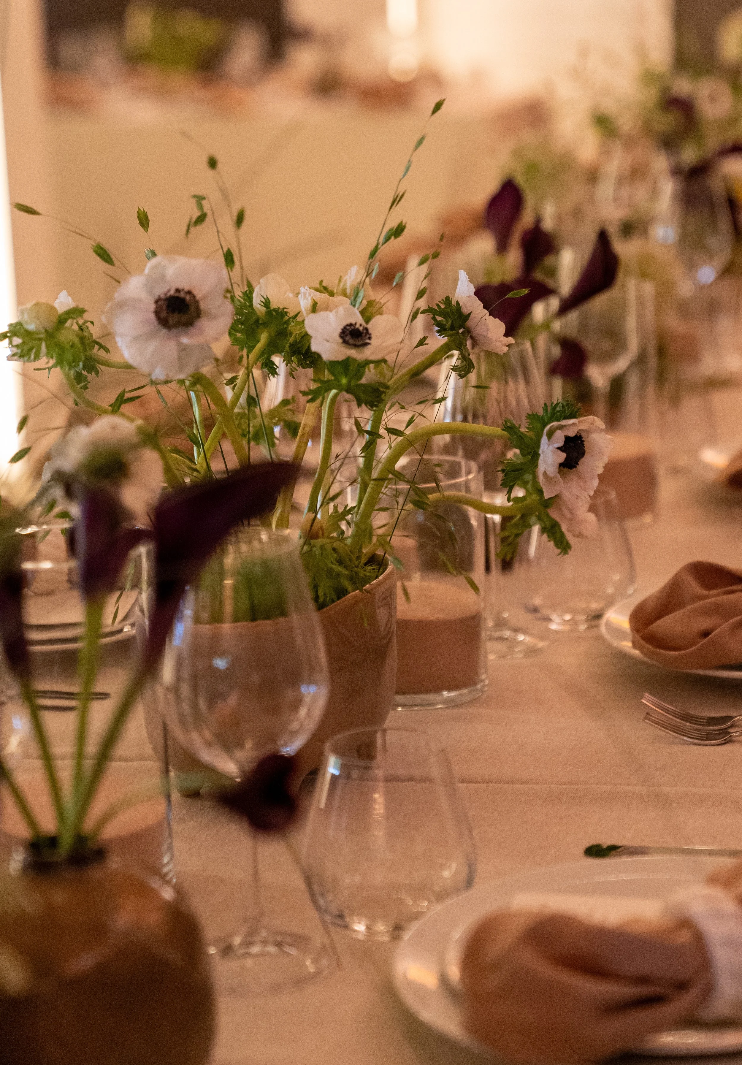 Vase avec des fleurs blanches, verre à vin, assiette avec un napperon en tissu beige, fourchette sur une nappe beige.