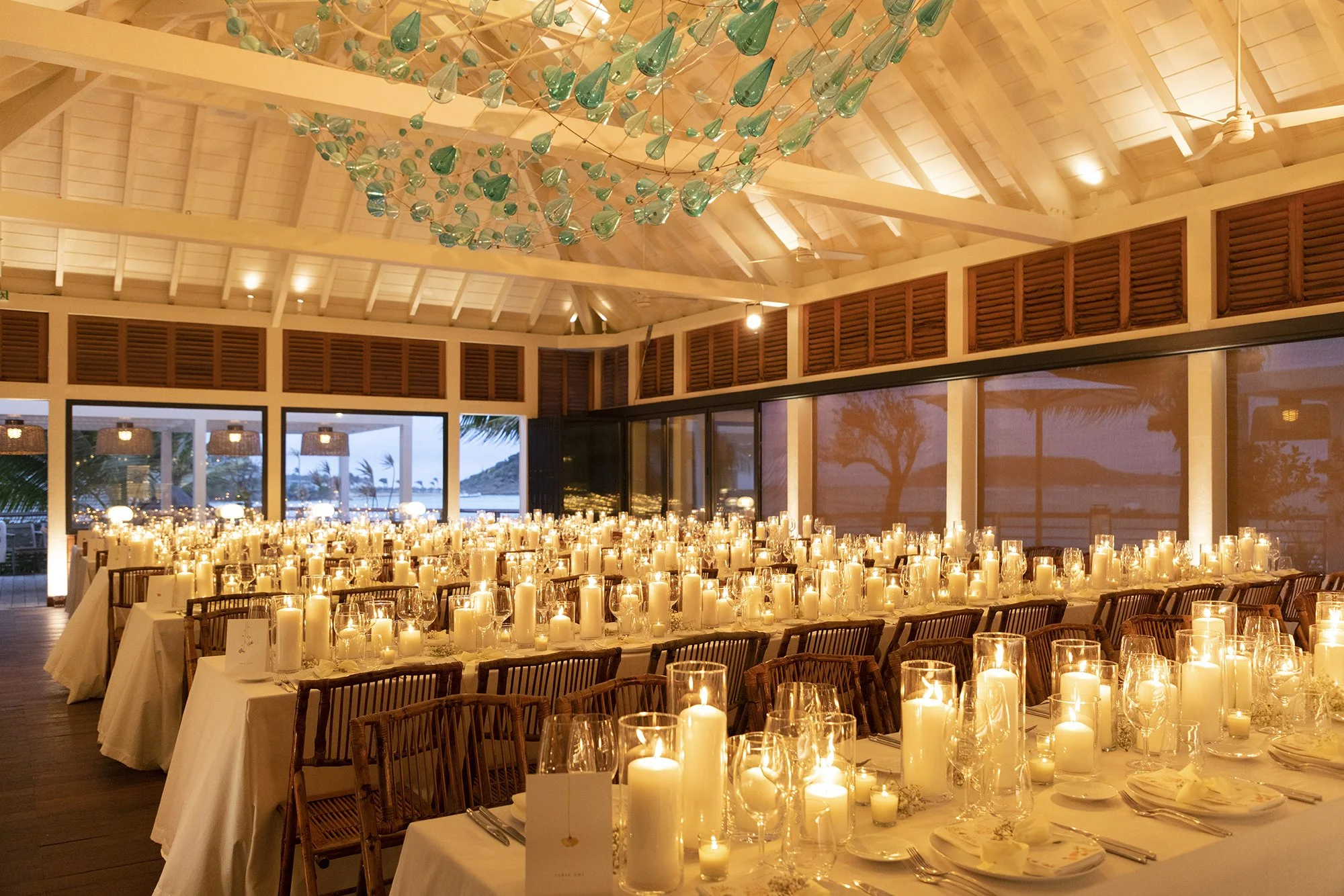 Elegant indoor wedding reception filled with candlelight, wooden chairs, and warm golden tones creating a romantic atmosphere in St Barth.