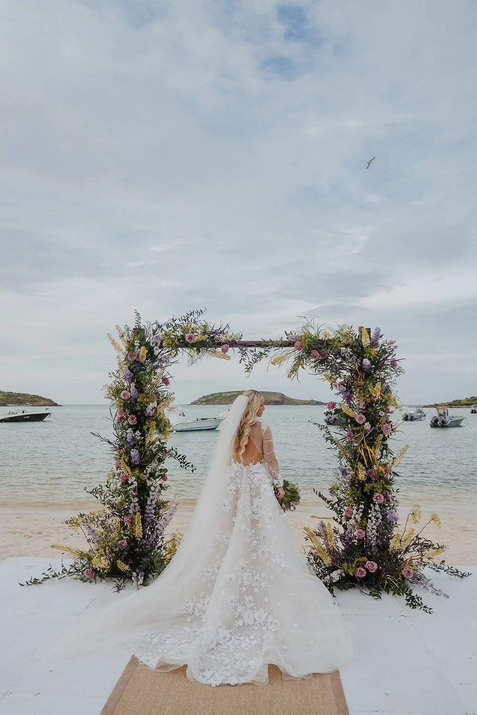Bride walking along a floral arch on the beach for a romantic seaside wedding ceremony in St Barth.
